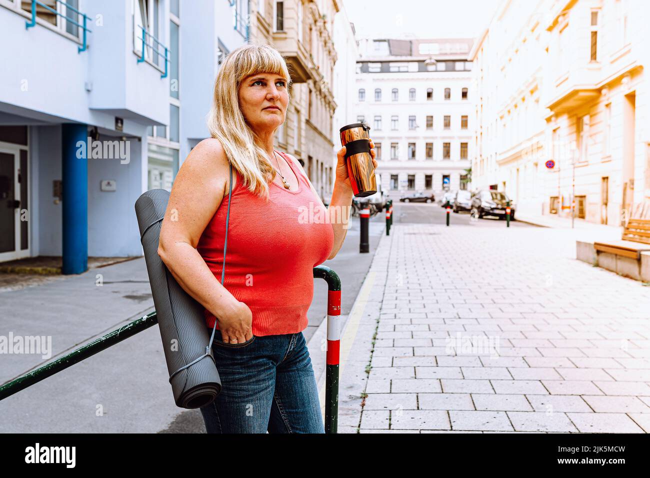 Mature happy middle aged woman 40s, long blond hair, smiling, big breasts,  in jeans, holding yoga mat, thermos in hands, against backdrop of European  Stock Photo - Alamy