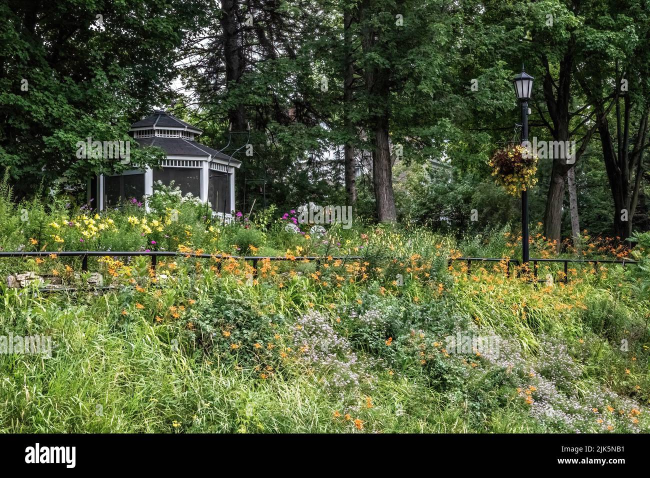 Hillside flower garden with orange daylilies with a gazebo and a lampstand with a hanging petunia flower basket. Stock Photo