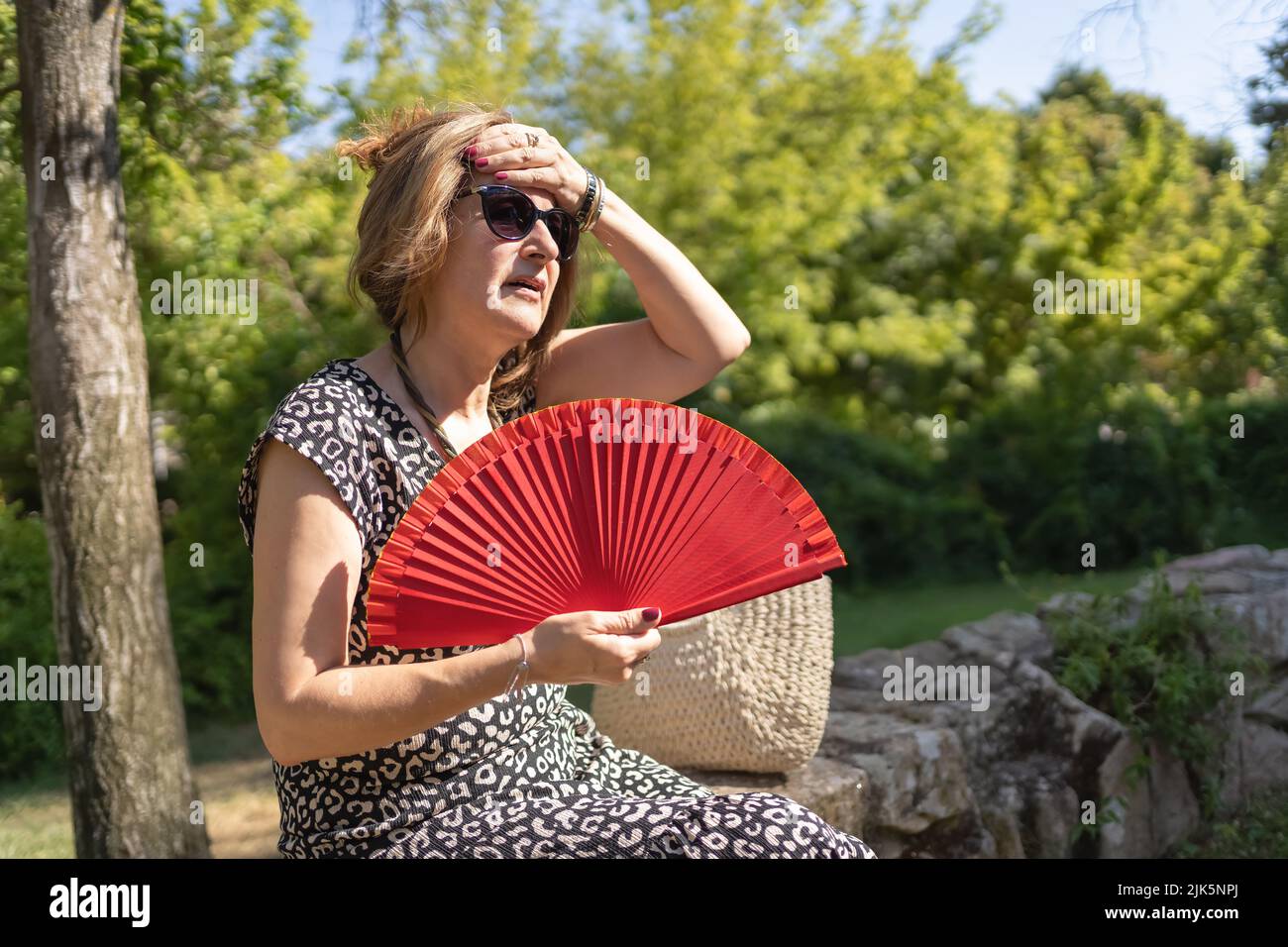 Mature woman fanning herself in the park by the strong summer heat wave. Stock Photo