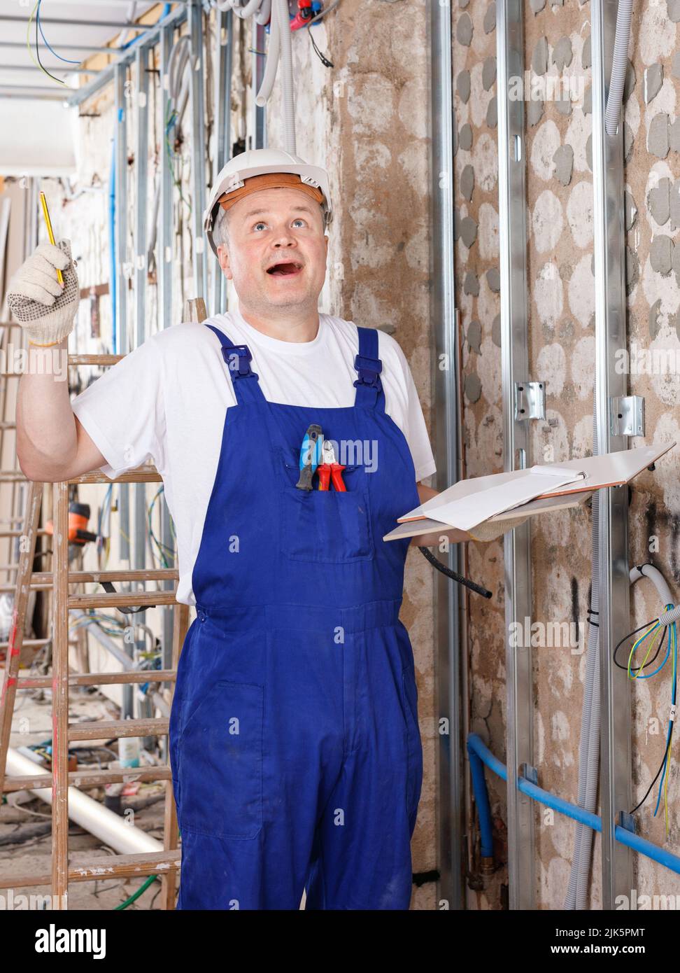 Happy contractor pointing pen up while planning building works, having good idea or smart construction solution Stock Photo