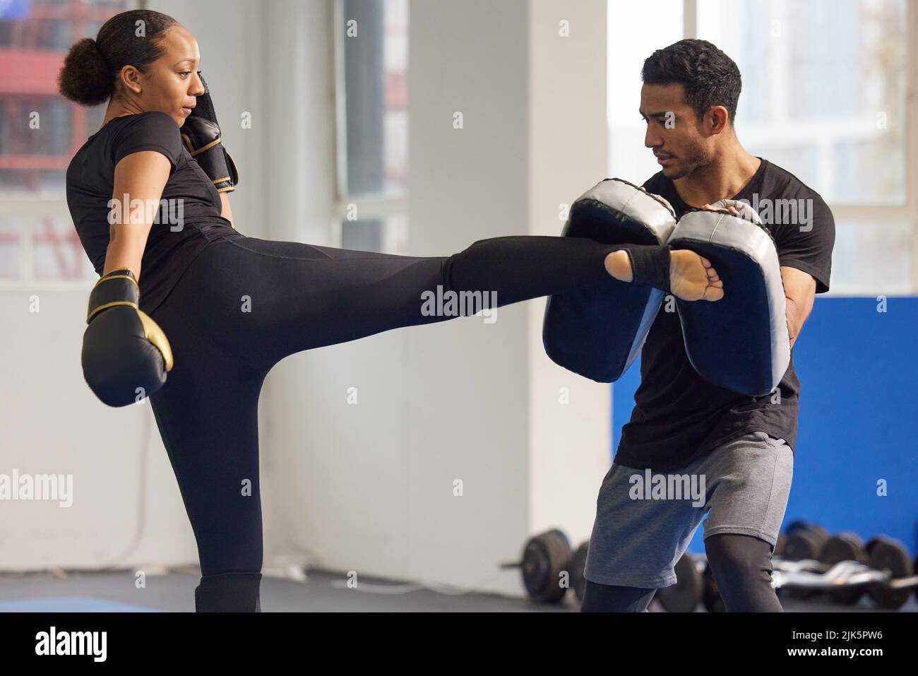 Gaining better balance, power and agility with every kick. a young woman practicing kickboxing with her trainer in a gym. Stock Photo