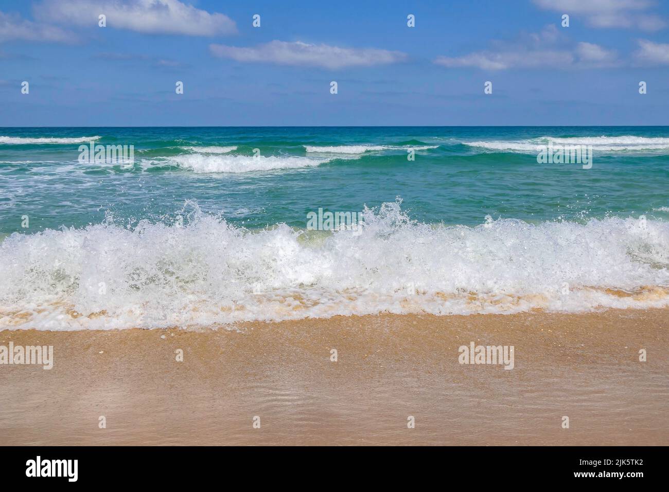 Foam and splashes on coastal waves. Sandy beach of the Mediterranean Sea. Stock Photo