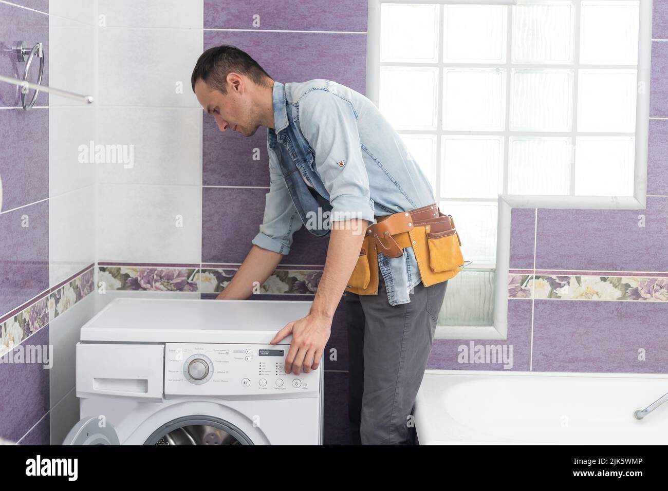 working man plumber repairs a washing machine in laundry Stock Photo