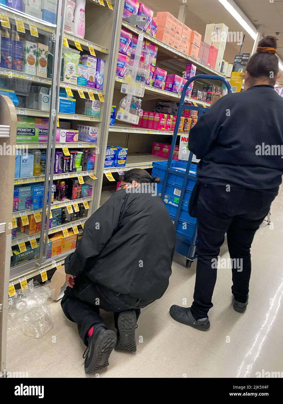 Tuscon, Arizona, USA. 15th July, 2022. Two Safeway employees in Tucson, Arizona restock shelves near the Pharmacy. Half are in locked cases due to high incidents of shoplifting all over the USA. One clerk knees in front of the condom shelf. (Credit Image: © Amy Katz/ZUMA Press Wire) Stock Photo