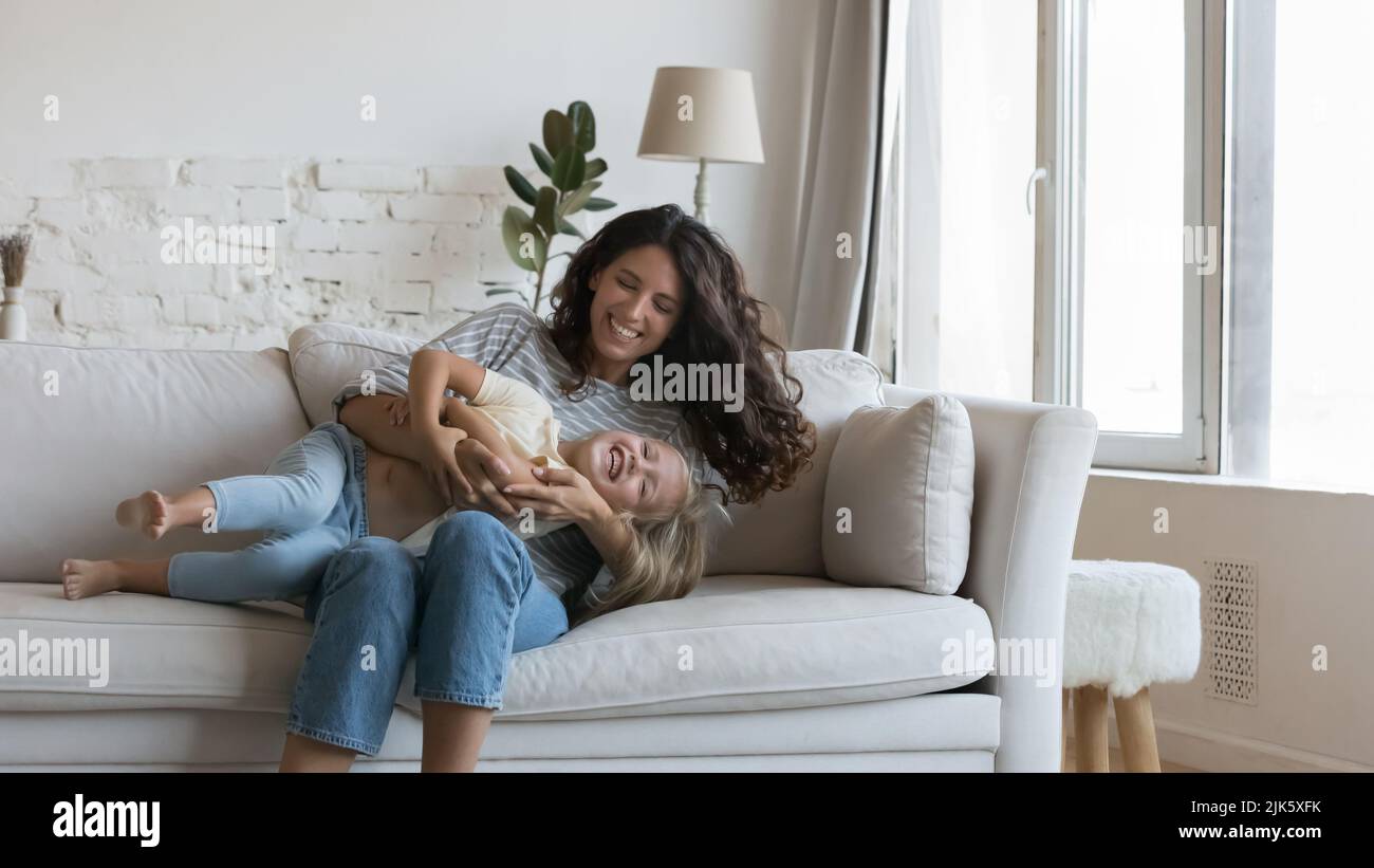 Cheerful happy mom cuddling cute little daughter kid on sofa Stock Photo