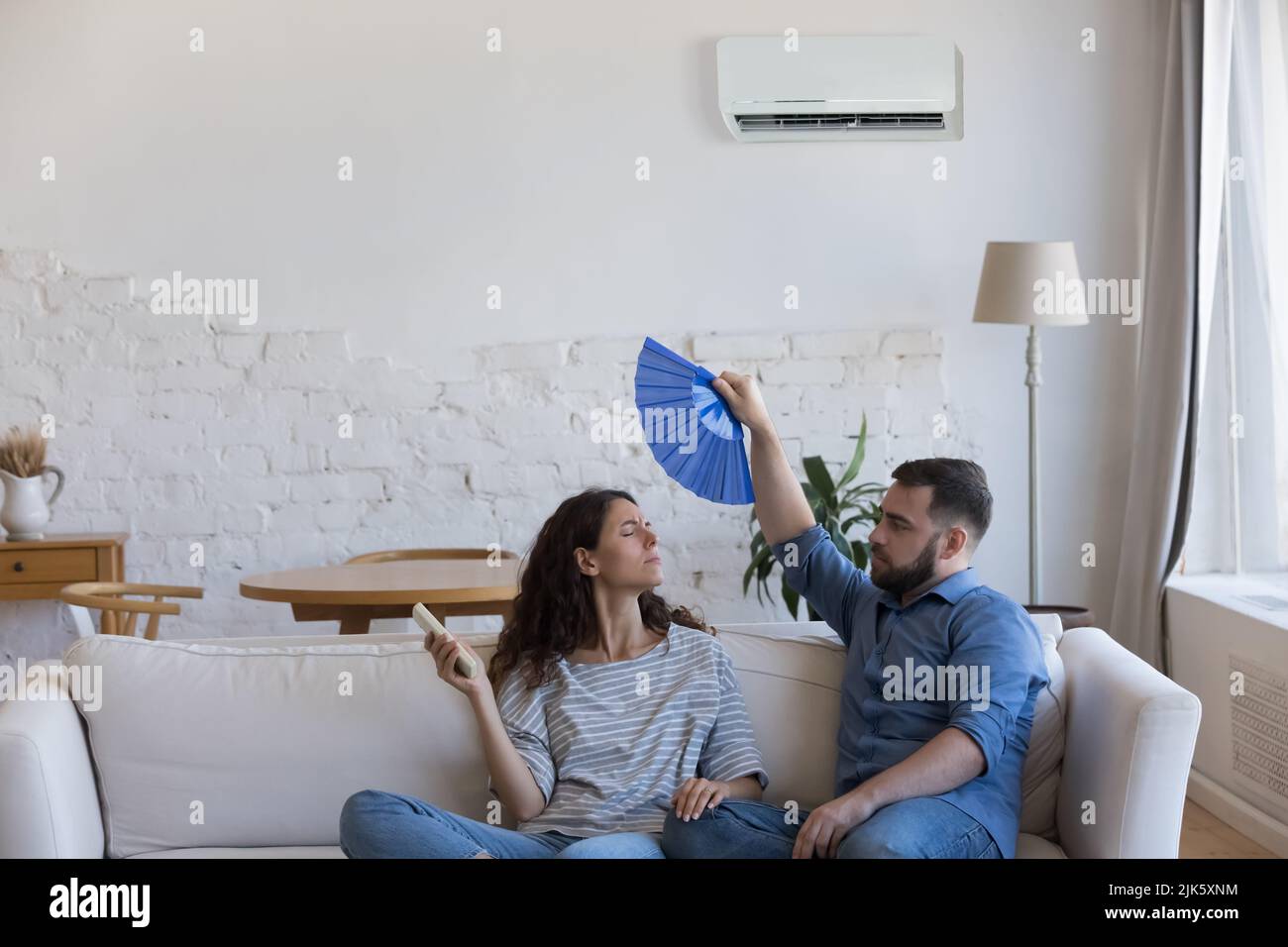 Young couple frustrated with heat, waving handheld fan Stock Photo
