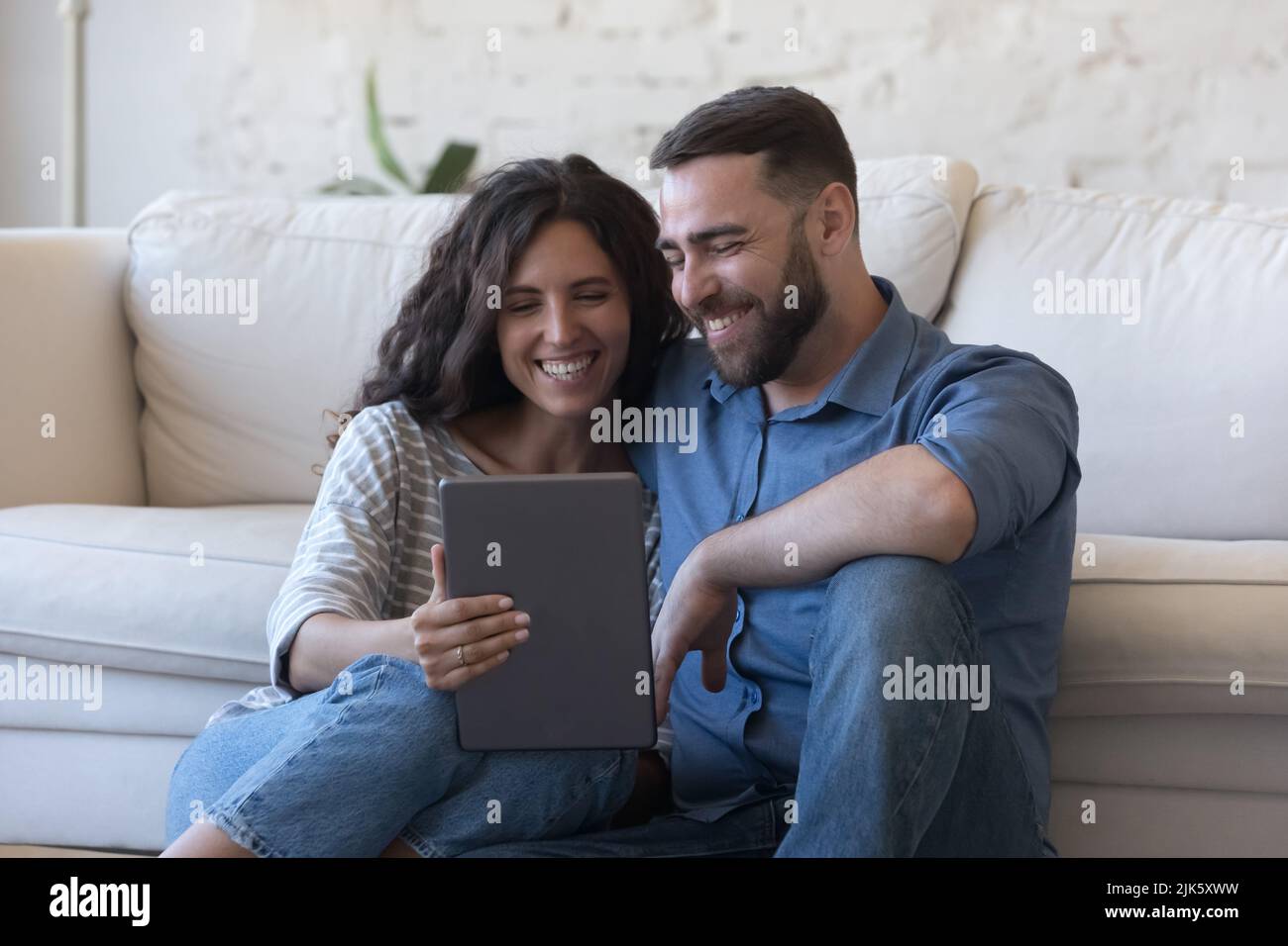 Cheerful couple of satisfied gadget users sitting on floor Stock Photo