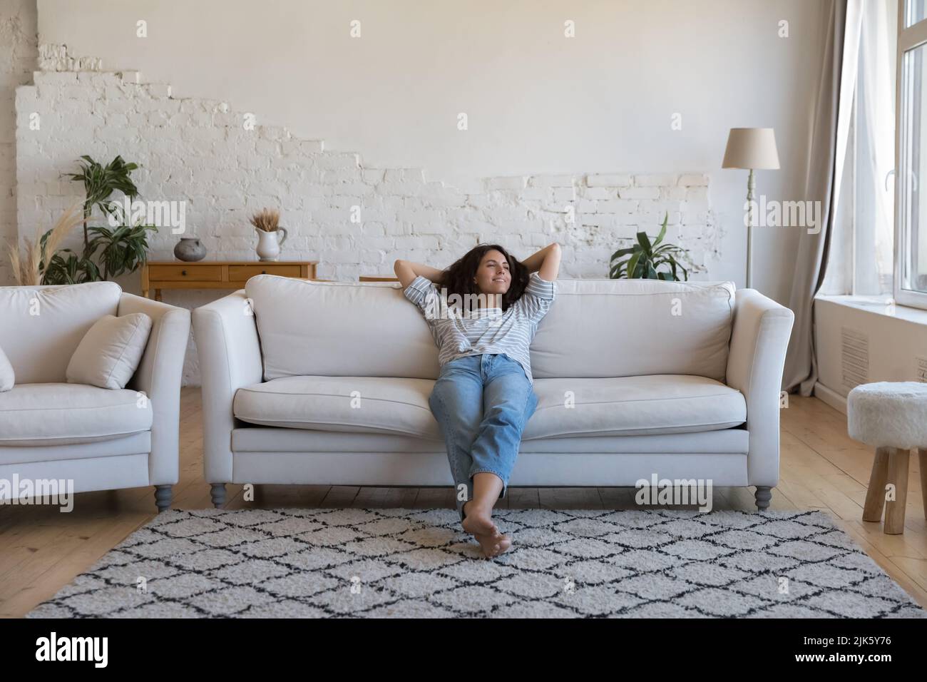 Happy thoughtful Latin woman resting on comfortable couch at home Stock Photo