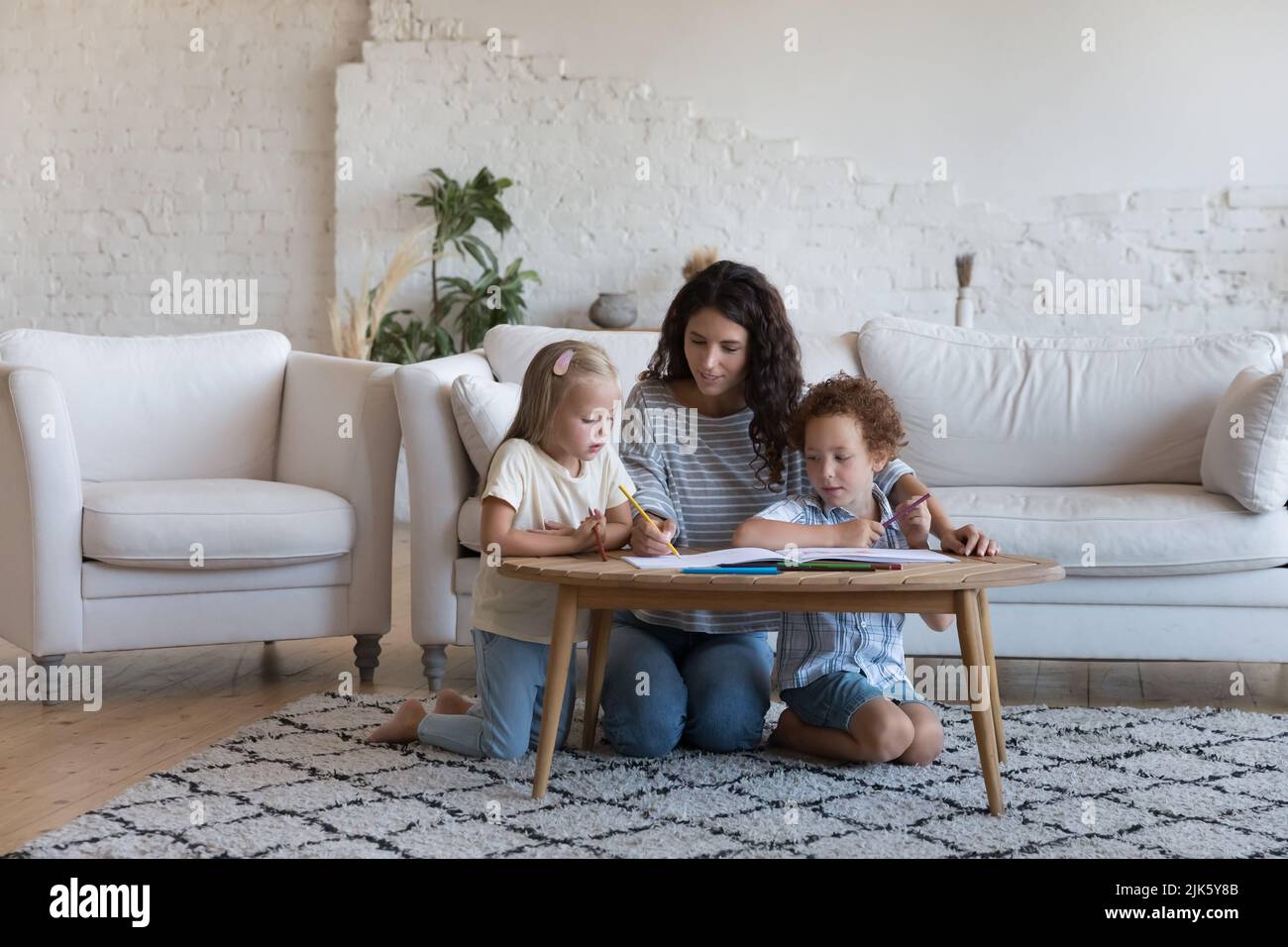 Mom teaching daughter and son kids to draw in pencils Stock Photo