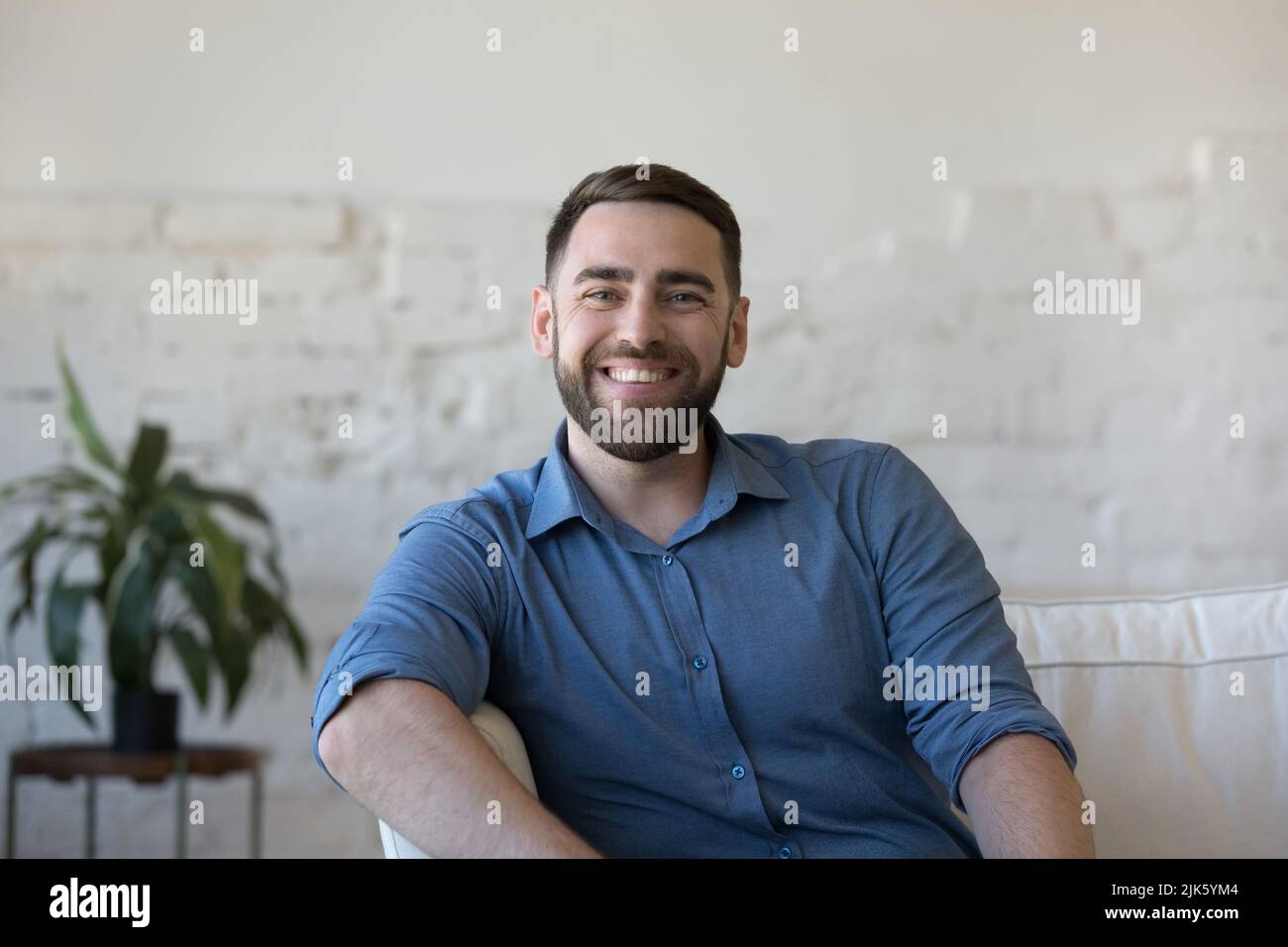 Happy handsome man sitting on home couch, looking at camera Stock Photo