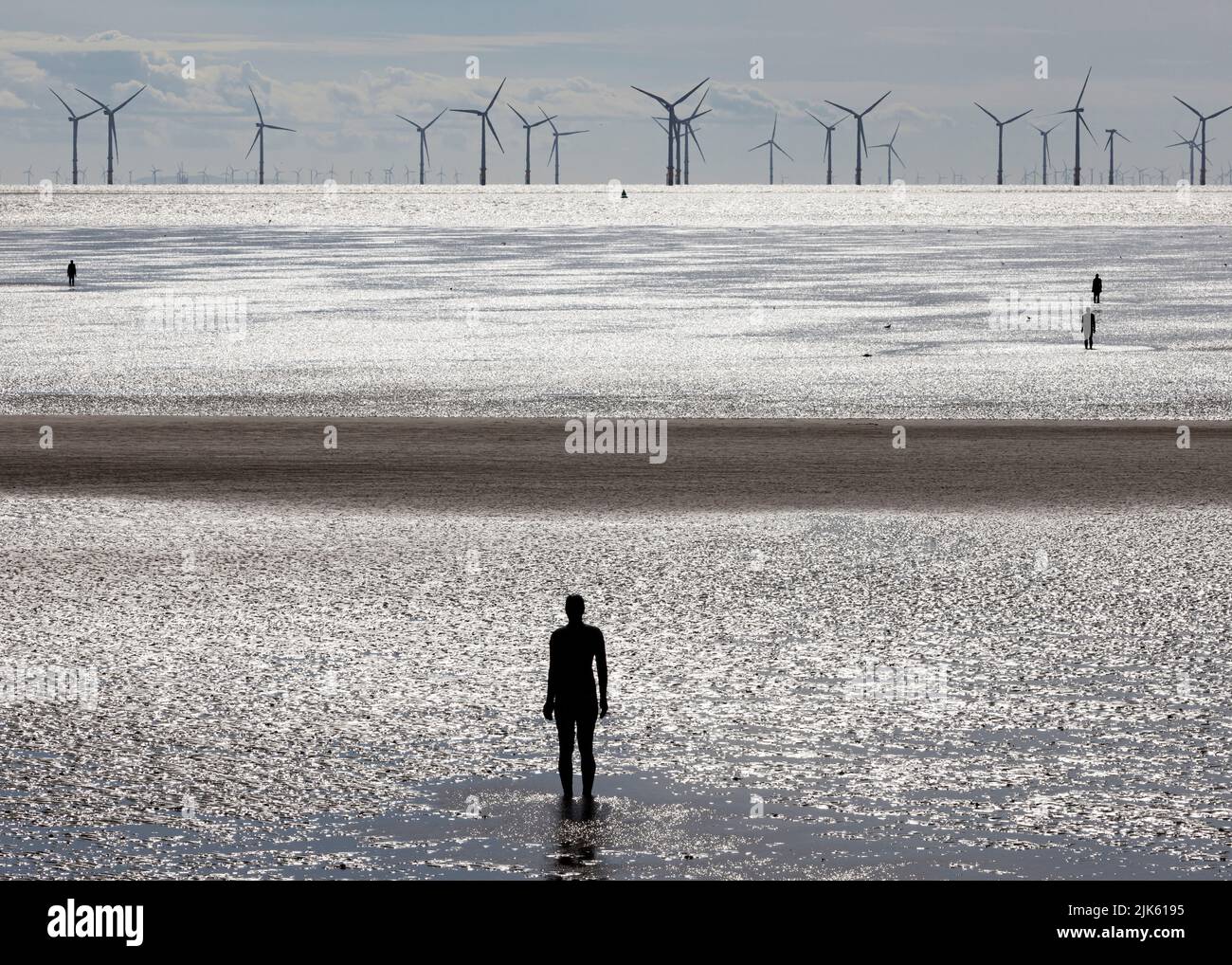 Another Place by Antony Gormley on Crosby Beach at low tide looking at a wind farm out at sea Stock Photo