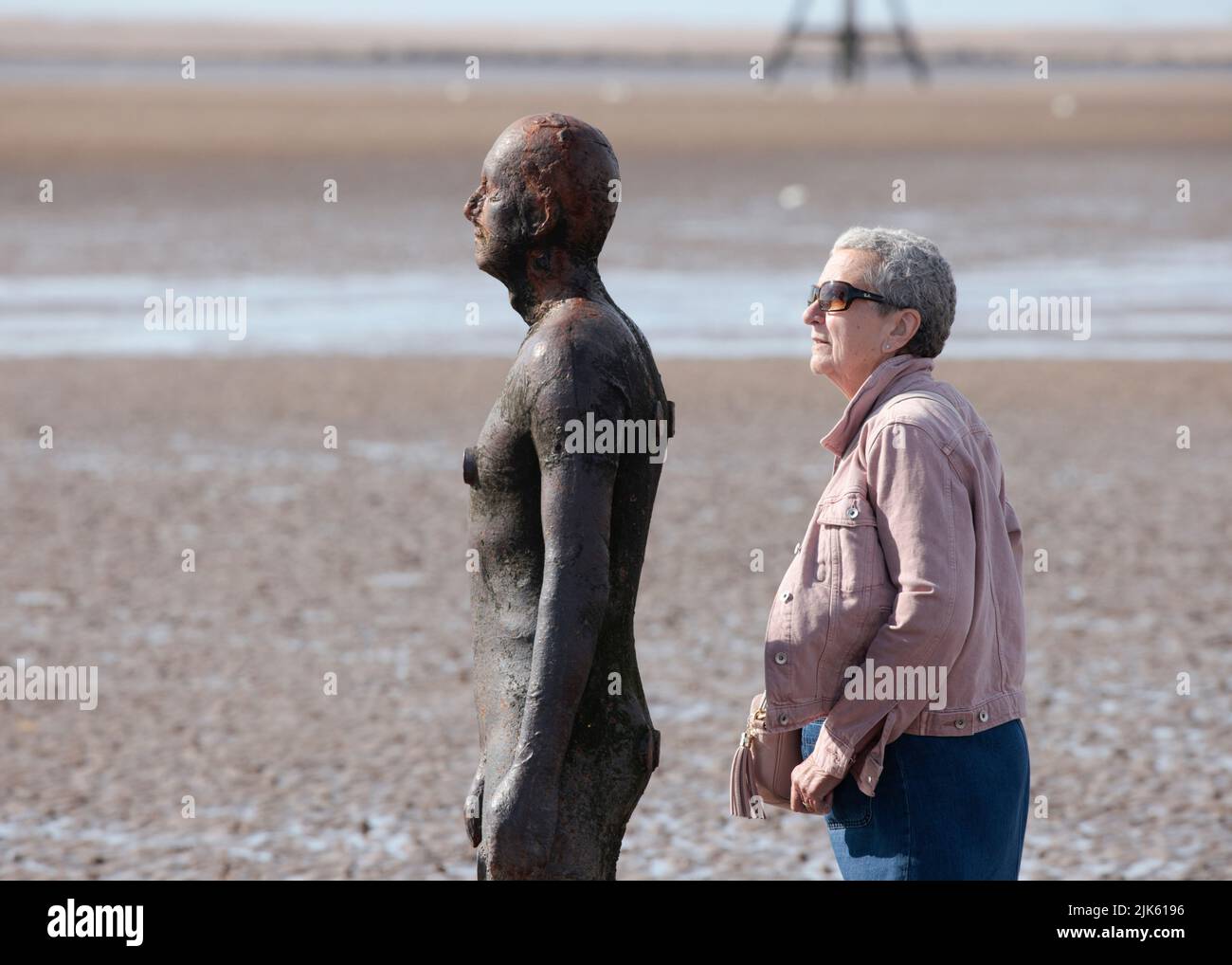Lady sharing the view of Another Place by Antony Gormley on Crosby Beach at low tide Stock Photo