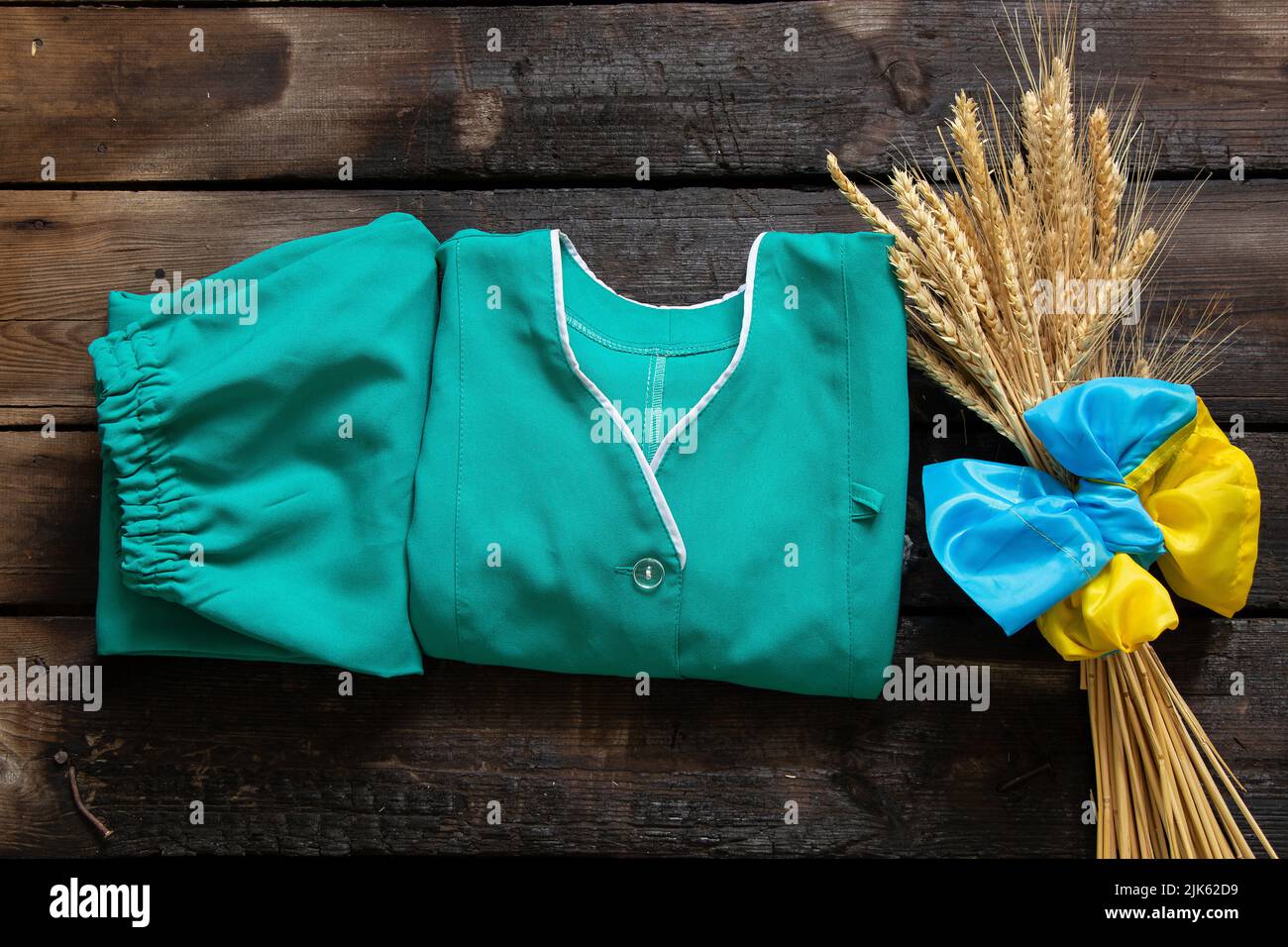 Spikelets of wheat and a medical gown and the flag of Ukraine lie on a hundred wooden table, profession, war in Ukraine Stock Photo