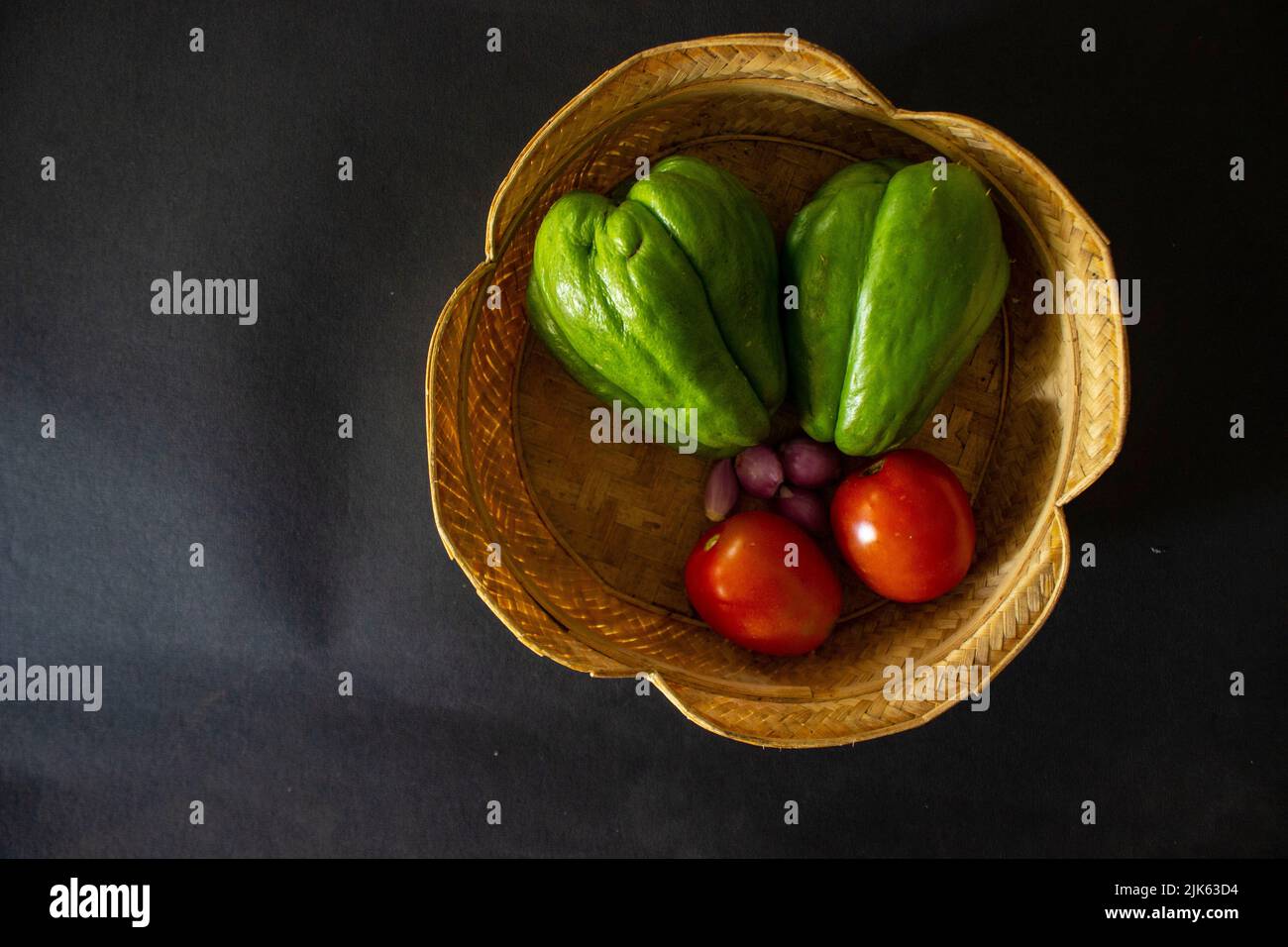 tropical tomatoes with jipang or labu siam or chayote and onion are served in a basket isolated on black background Stock Photo