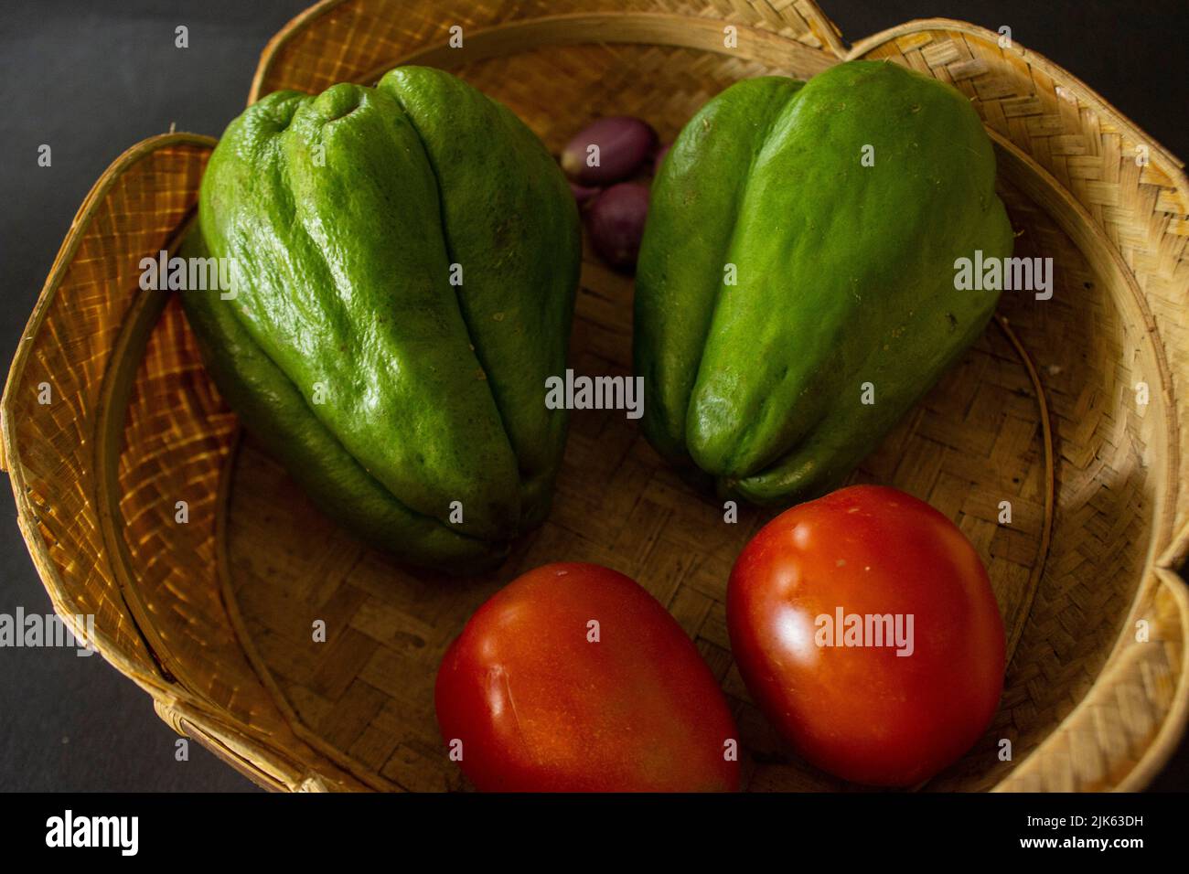 tropical tomatoes with jipang or labu siam or chayote and onion are served in a basket isolated on black background Stock Photo