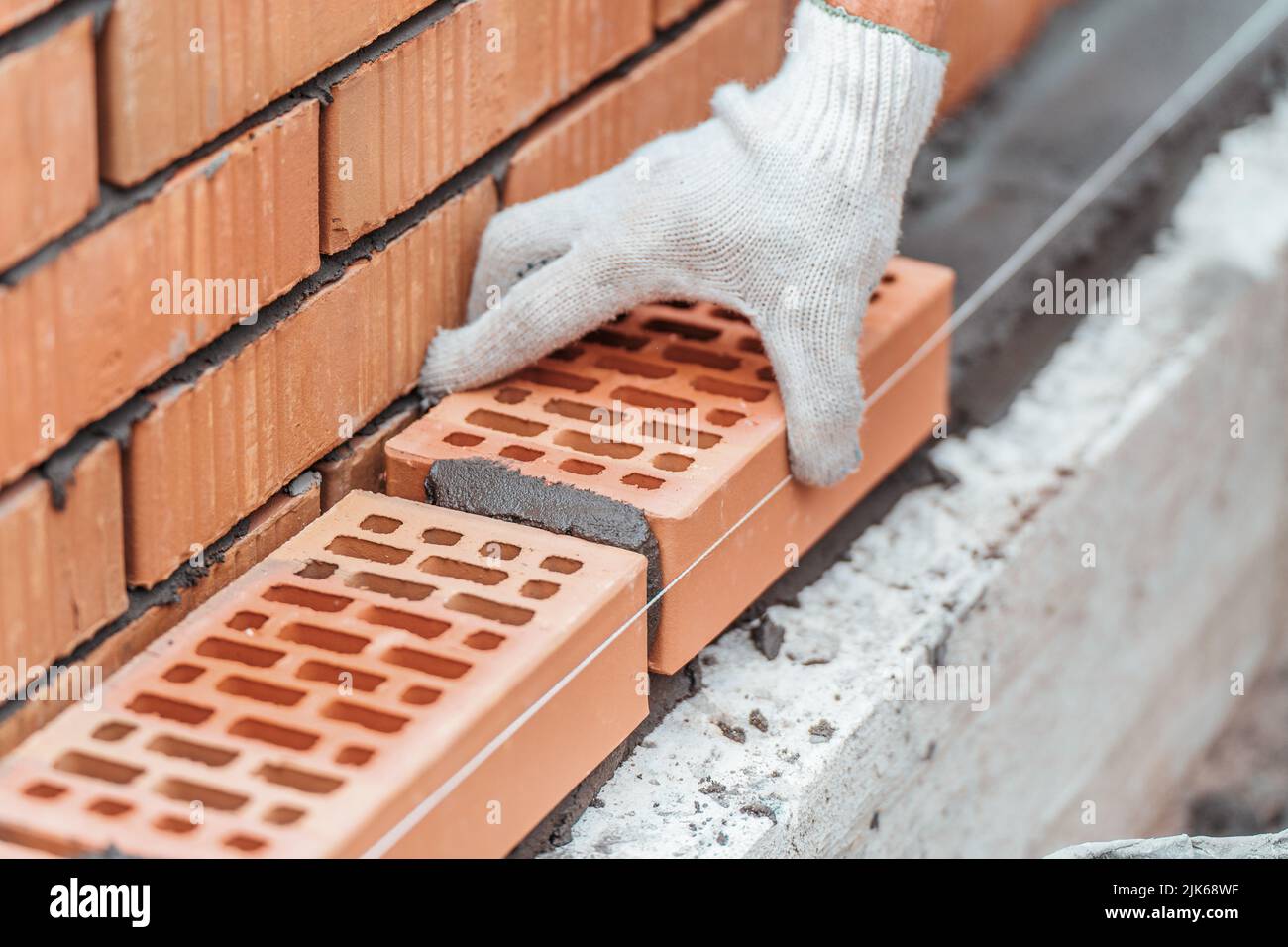 Worker lays brick on cement mortar. Construction of brick fence. Bricklayer at work. Stock Photo