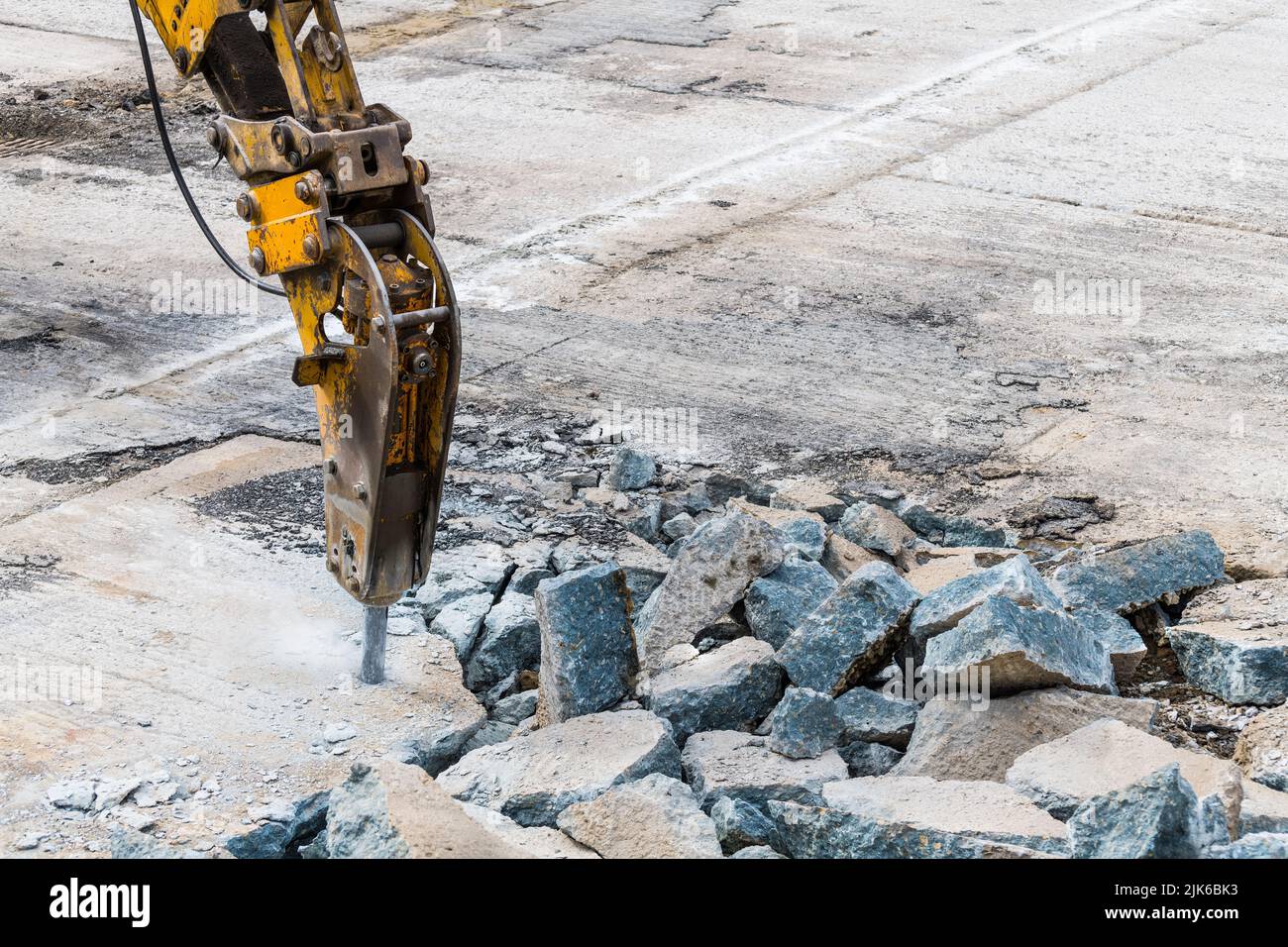 Excavator mounted hydraulic jackhammer at breaking a concrete area. Closeup of working demolition hammer. Heavy equipment detail on construction site. Stock Photo
