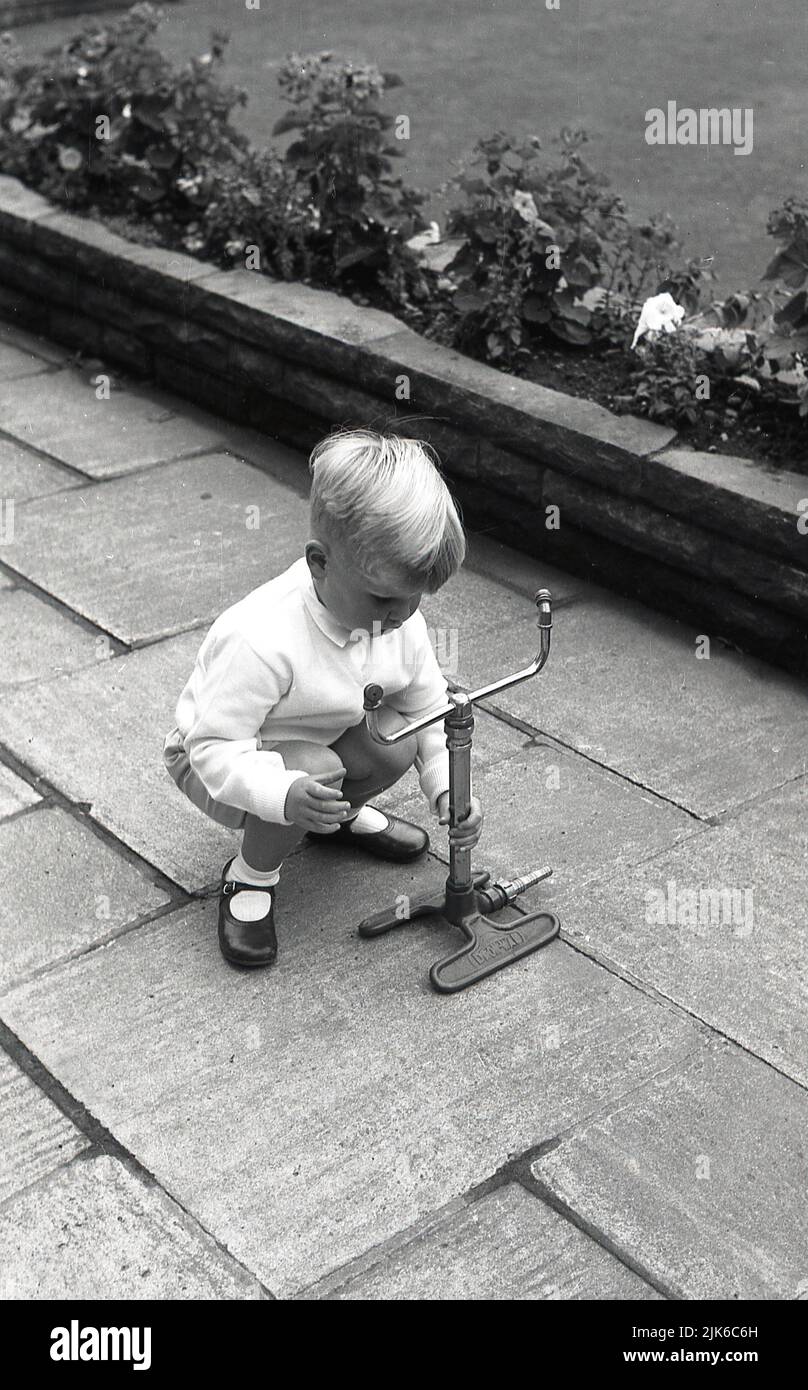1960s, historical, outside on a garden patio, a young boy playing with a metal framed twin bunsner?? burber, Dron-Wad??? Stock Photo