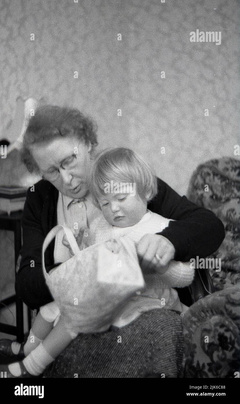 1960s, historical, inside a front room, a little girl sitting on her grandma's lap looking through her handbag, England, UK. Stock Photo