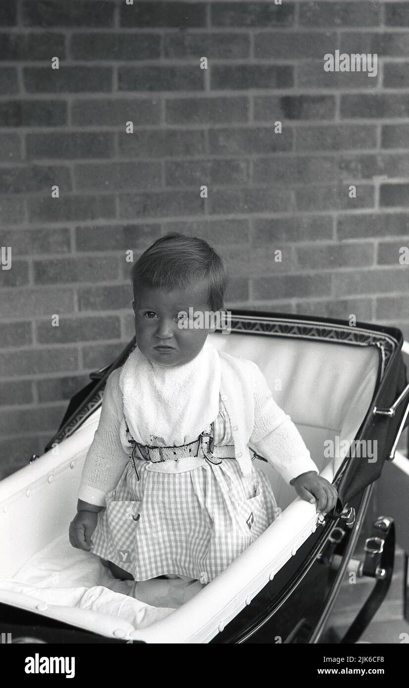 1960s, historical, strapped in with a harness, a soulful looking infant child kneeling in a traditional coach-built pram of the era, England, UK. Stock Photo
