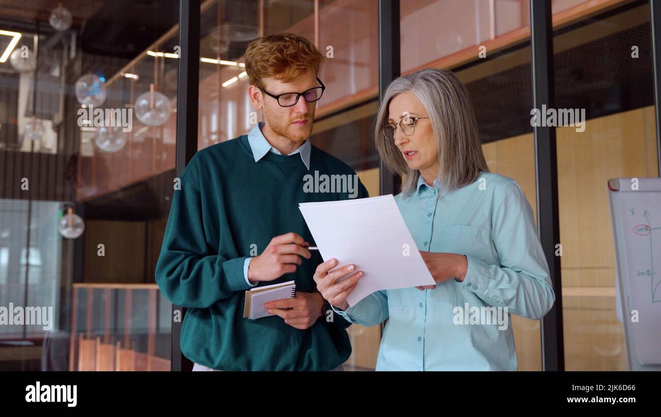 Mature businesswoman teaching on documents young male intern in office Stock Photo
