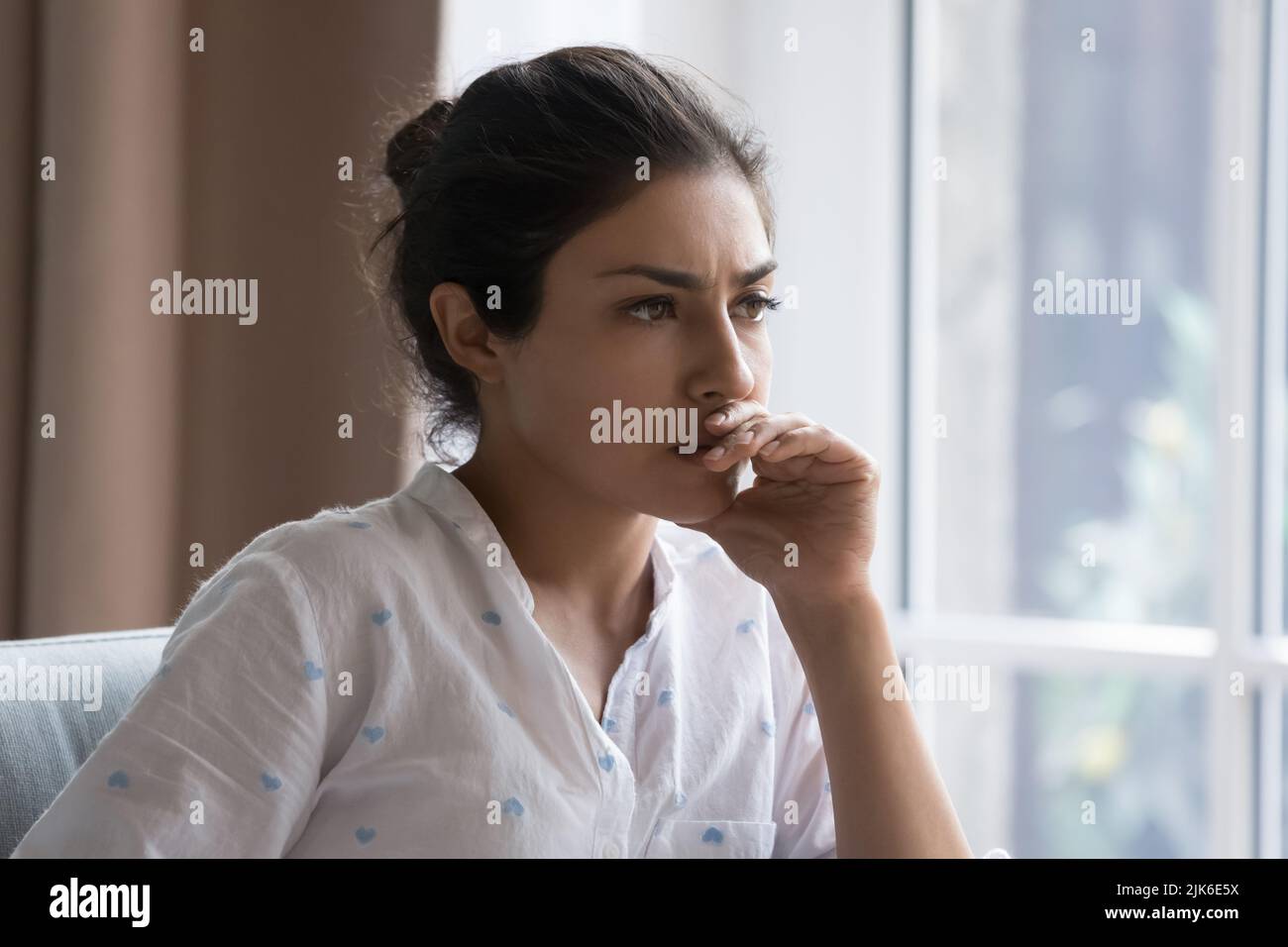 Serious thoughtful beautiful Indian woman sitting on couch indoors Stock Photo