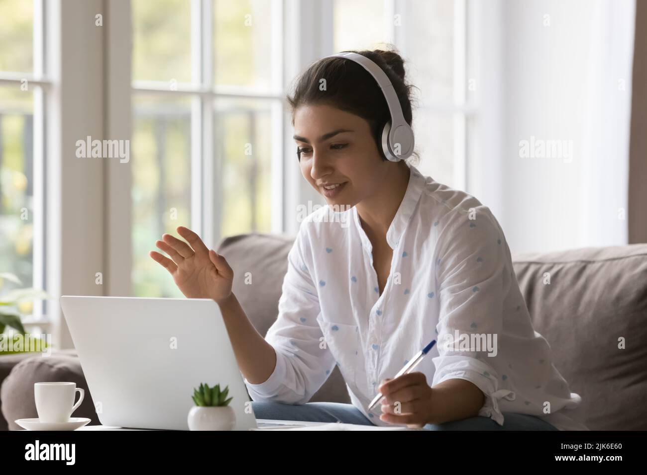 Positive Indian student girl in wireless headphones making video call Stock Photo