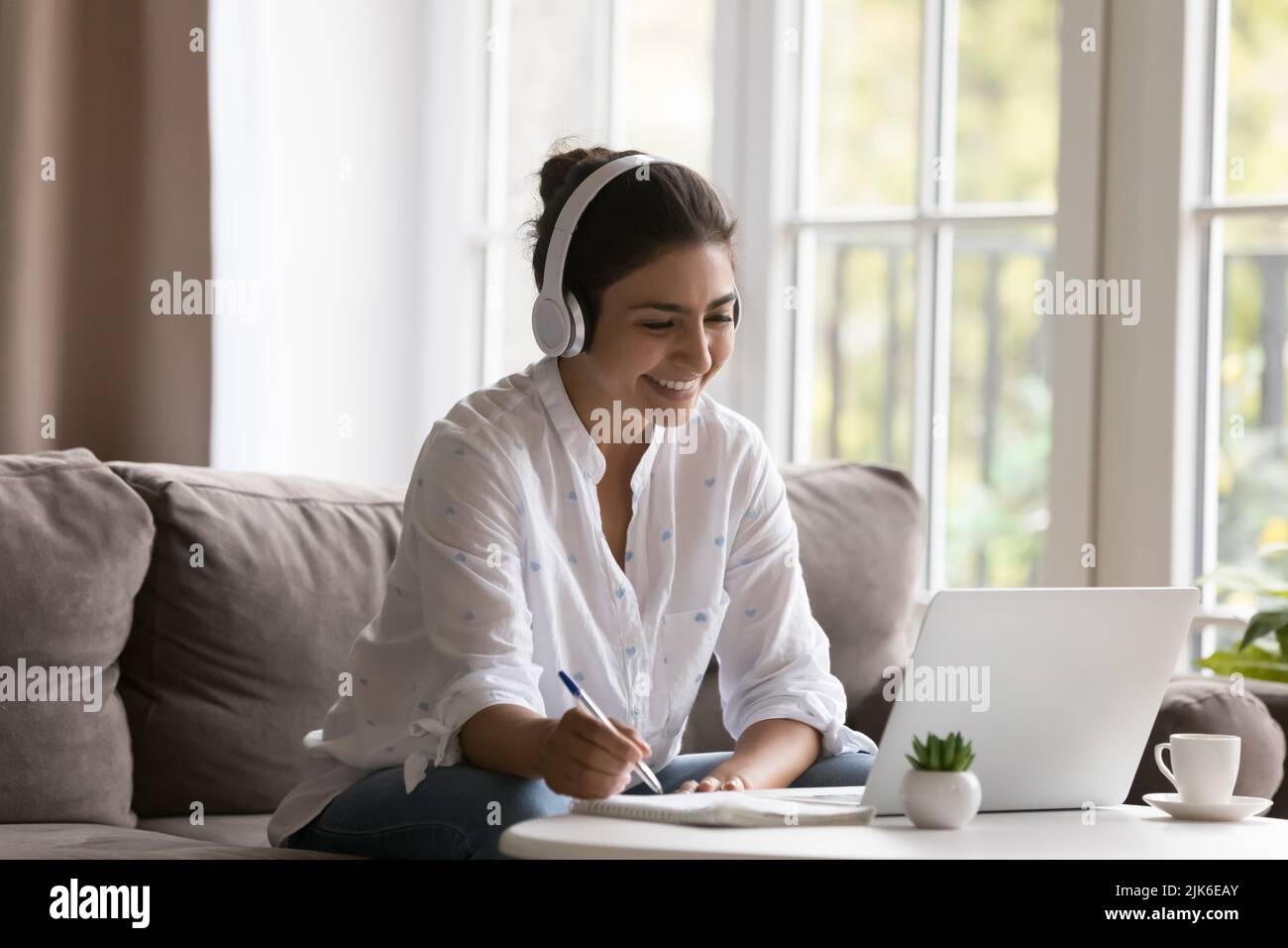 Happy young Indian student woman in wireless headset watching webinar Stock Photo