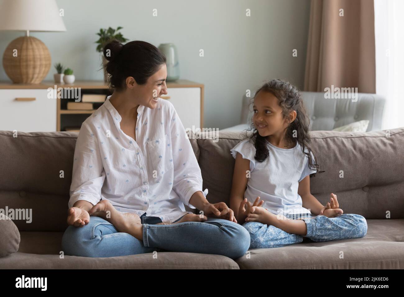 Cheerful Indian mom teaching girl to do yoga at home Stock Photo