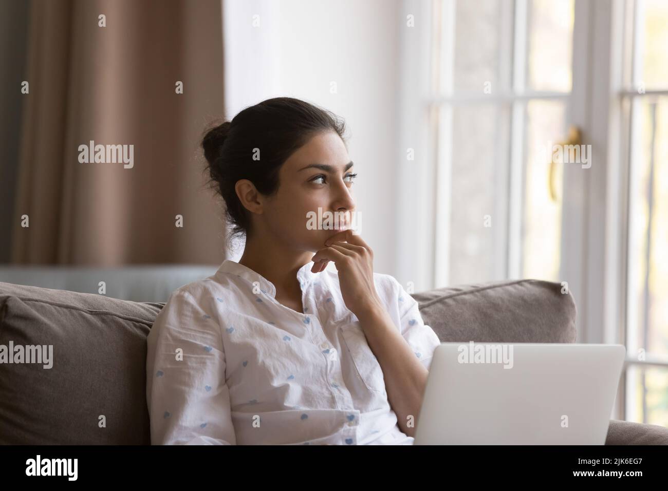 Dreamy beautiful young Indian woman holding laptop on lap Stock Photo