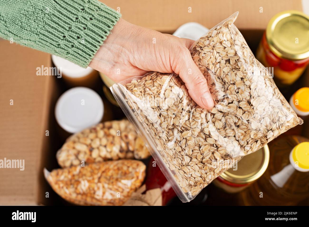 Plastic container with rolled oats in female hand on emergency food box background Stock Photo
