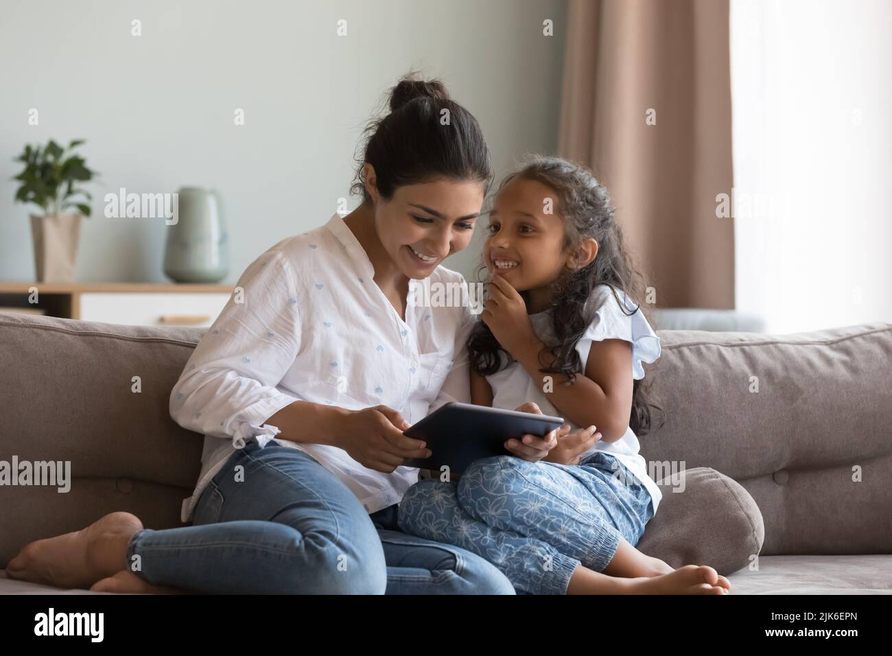 Happy Indian little daughter kid talking to mom, using tablet Stock Photo