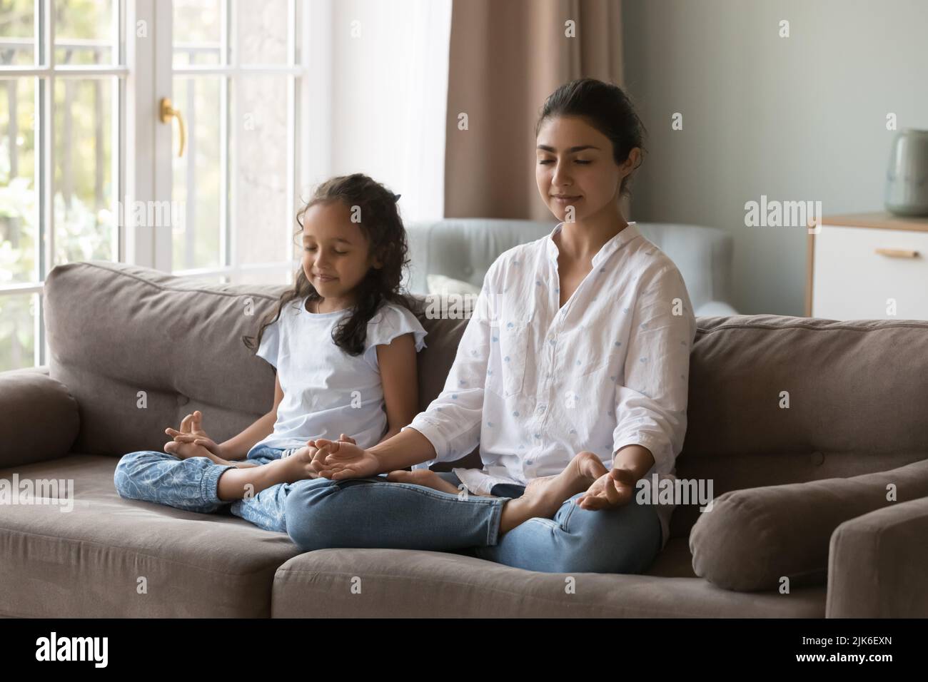 Peaceful young Indian mother teaching girl to meditate at home Stock Photo