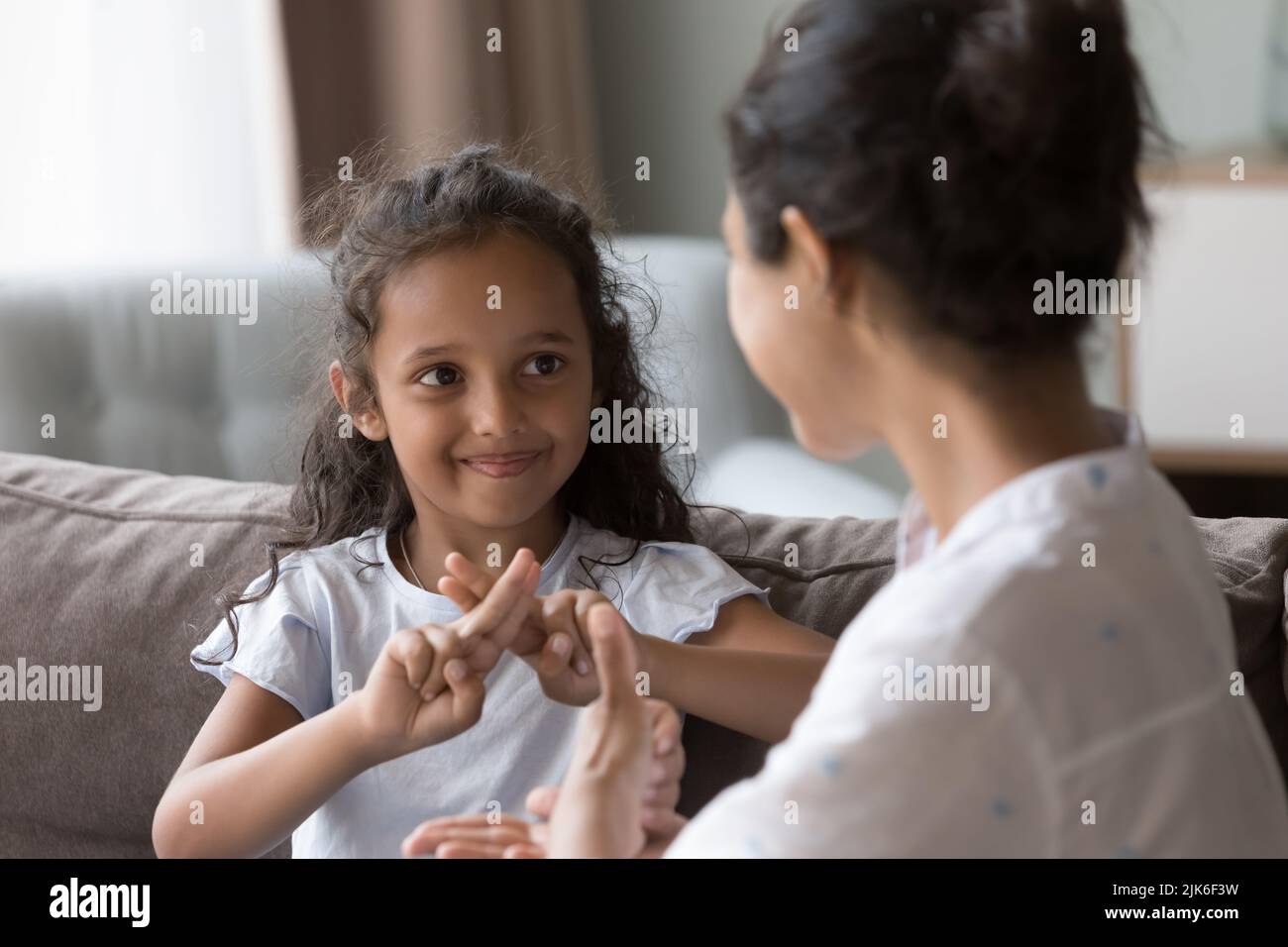 Happy cute Indian kid girl talking to mother, using hands Stock Photo