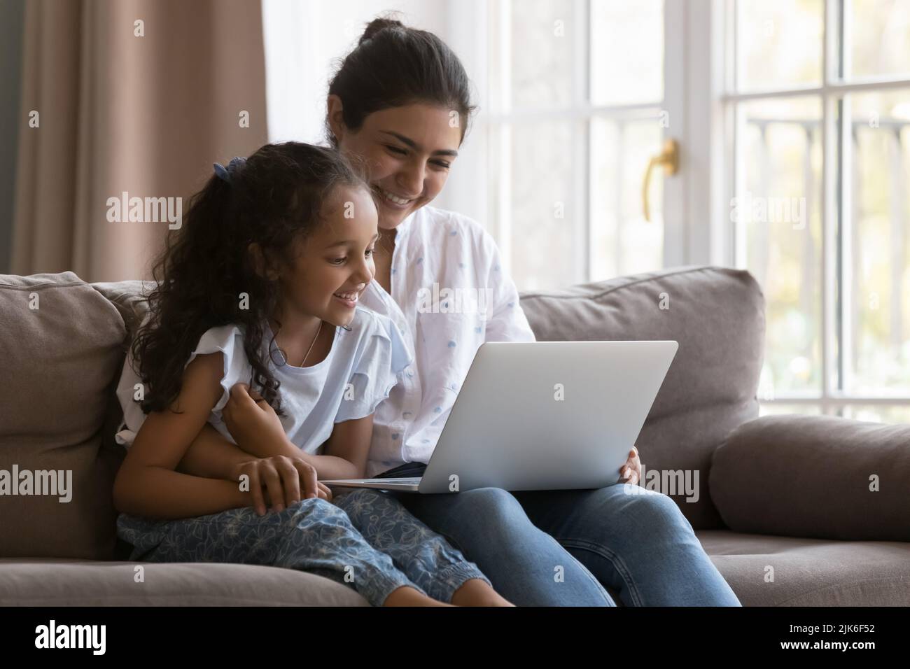 Happy young Indian mother and curious kid watching movie Stock Photo