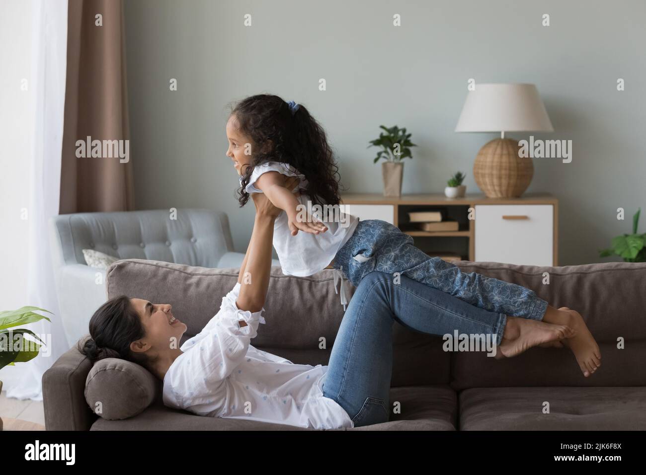 Excited active Indian mom playing airplane with cute little kid Stock Photo