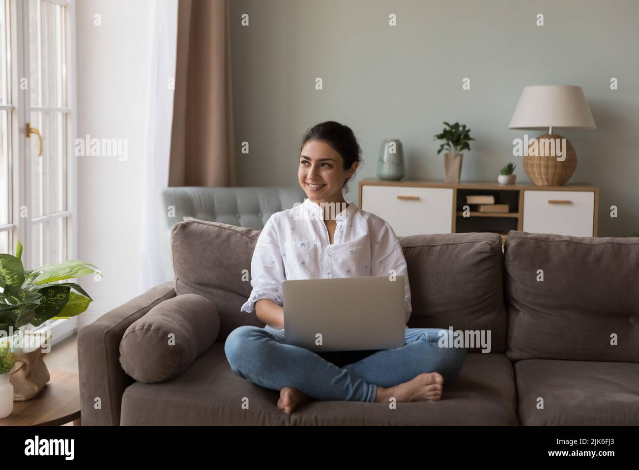 Cheerful happy Indian woman holding laptop, sitting on comfortable couch Stock Photo