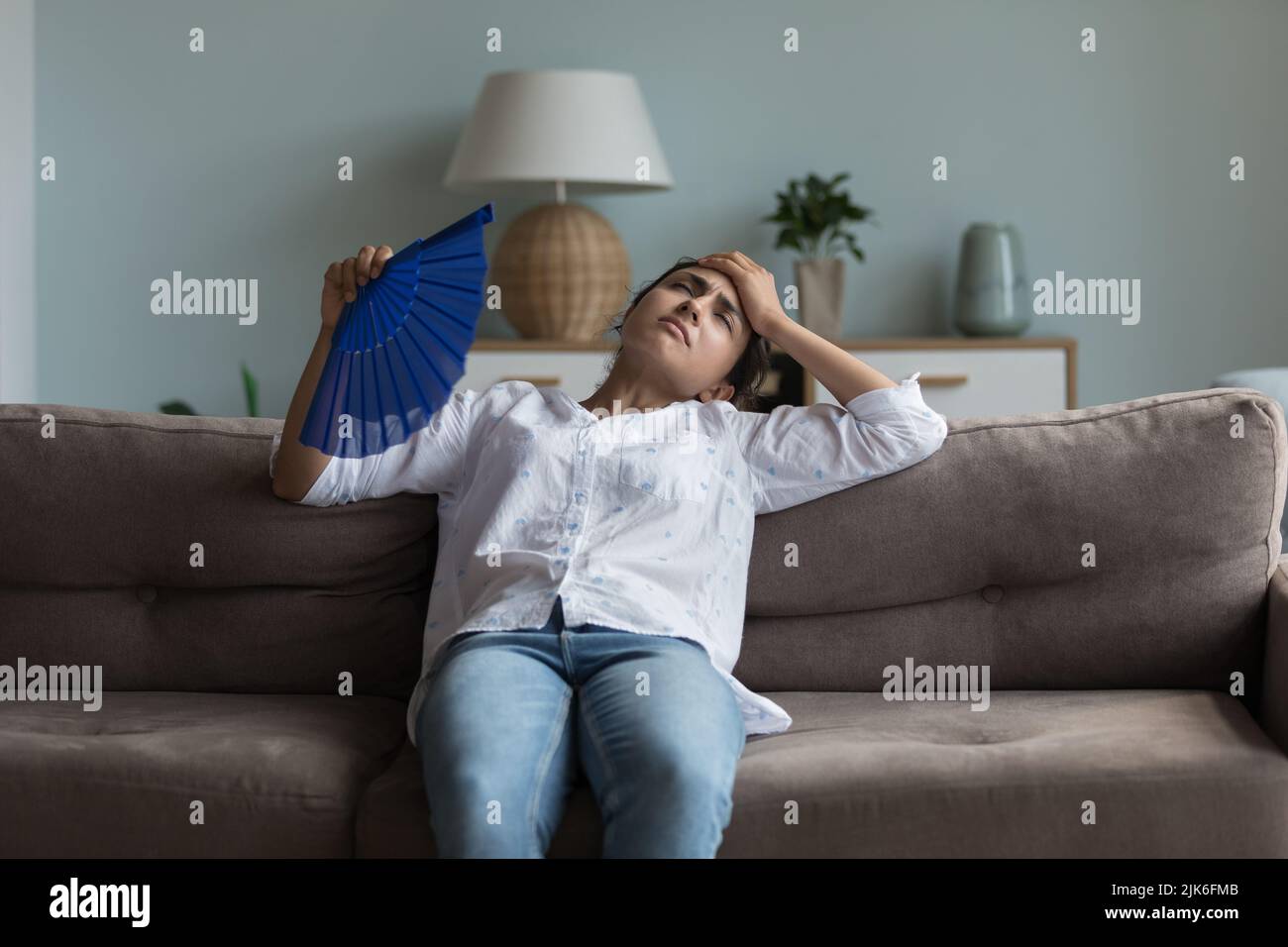 Exhausted young Indian girl feeling hot, resting on couch Stock Photo