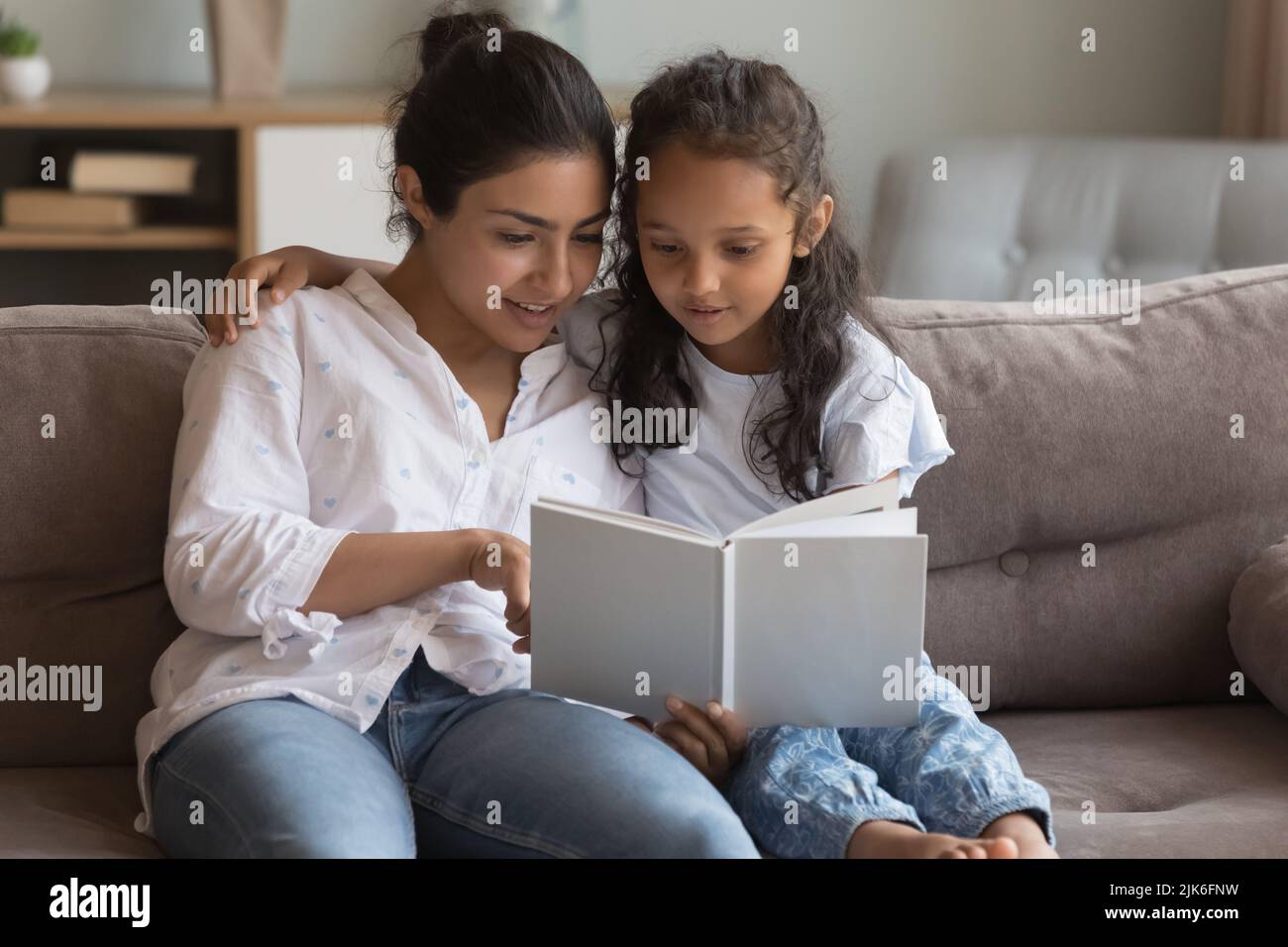 Happy young Indian mom teaching little daughter to read book Stock Photo