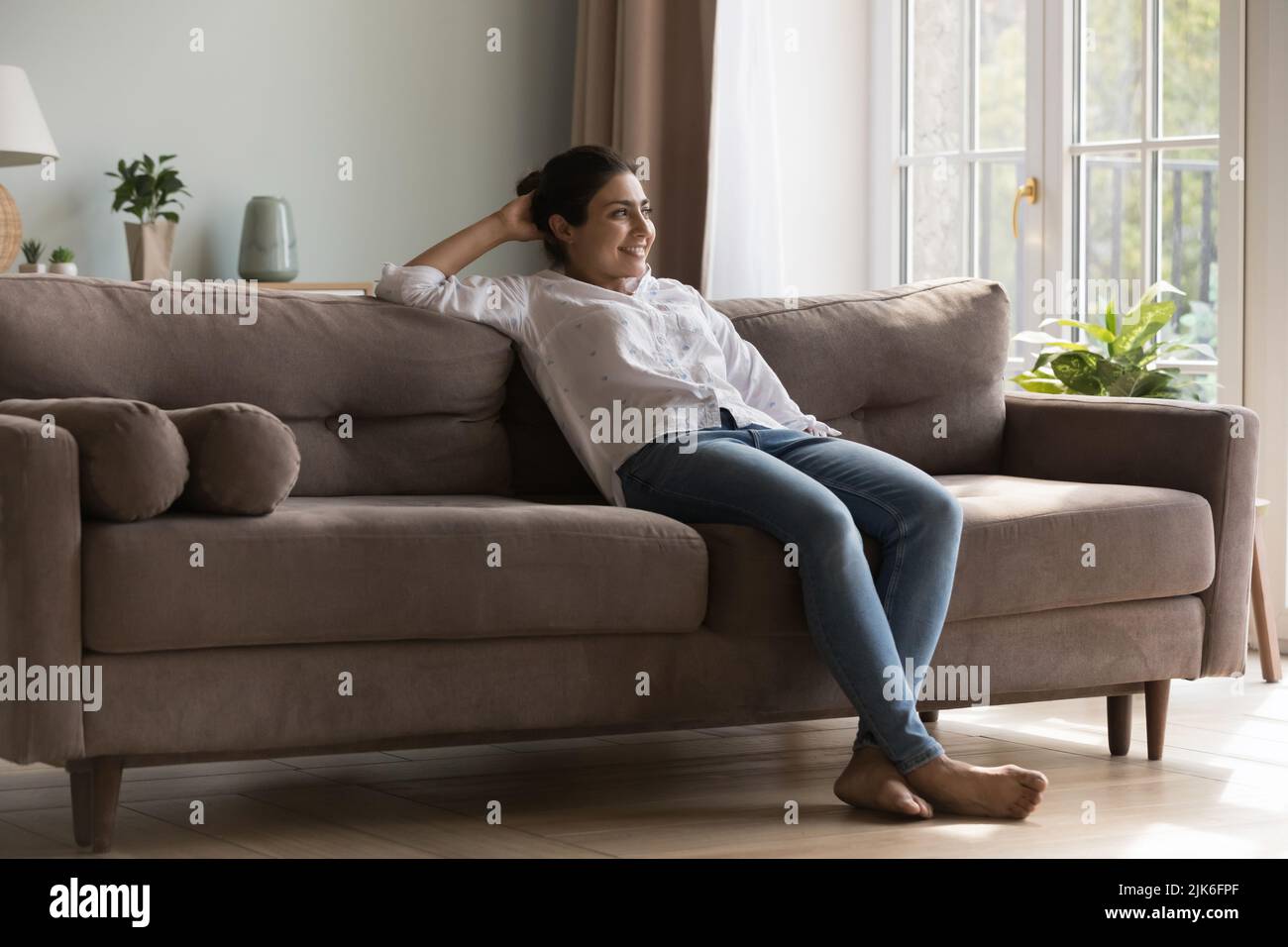 Cheerful carefree young Indian woman enjoying relaxation co comfortable sofa Stock Photo