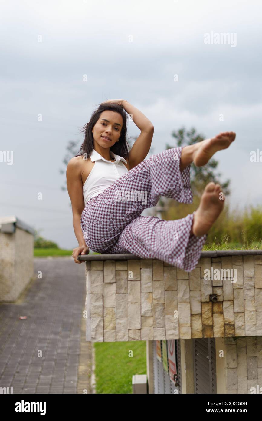 full body of a young woman with short hair sitting with her legs raised, she wears comfortable clothes and is barefoot, lifestyle and beauty Stock Photo