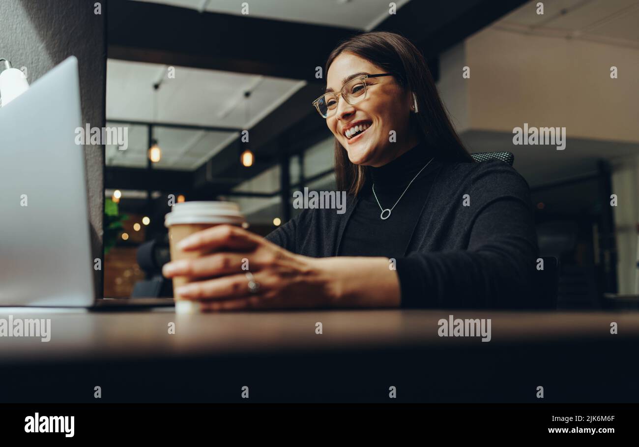 Businesswoman smiling cheerfully during an online meeting in a modern co-working office. Happy female entrepreneur communicating with her business ass Stock Photo