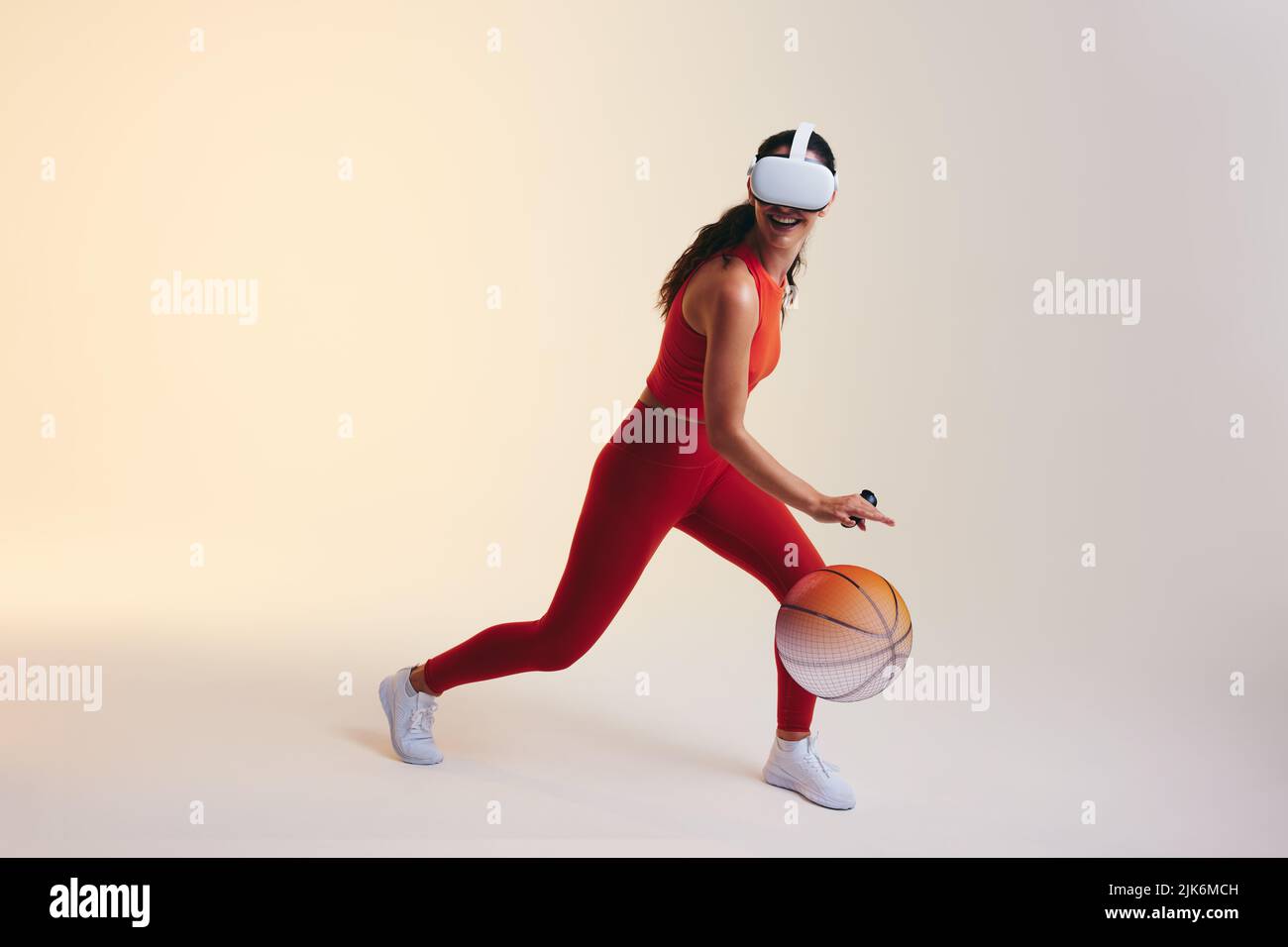 Happy young woman playing basketball in virtual reality. Sporty young woman smiling cheerfully while bouncing a virtual ball. Athletic young woman wea Stock Photo