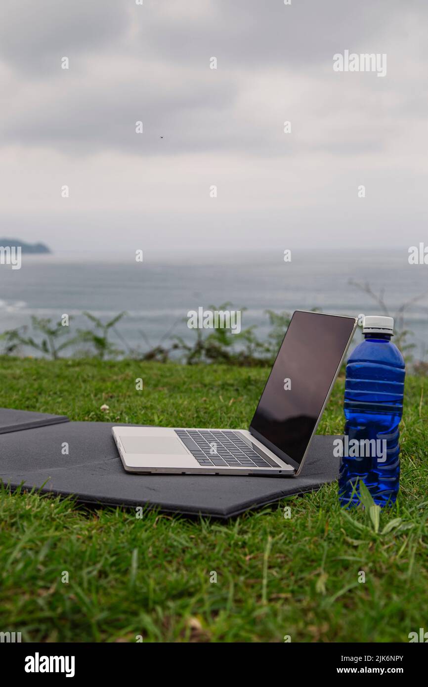 Online sports or yoga training concept Laptop with yoga mat, bottle of water outdoors Stock Photo