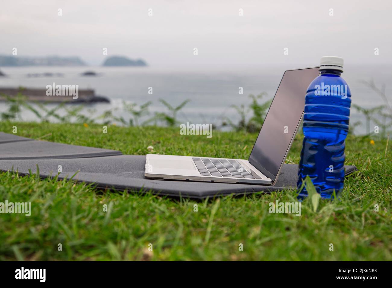 Online sports or yoga training concept Laptop with yoga mat, bottle of water outdoors Stock Photo
