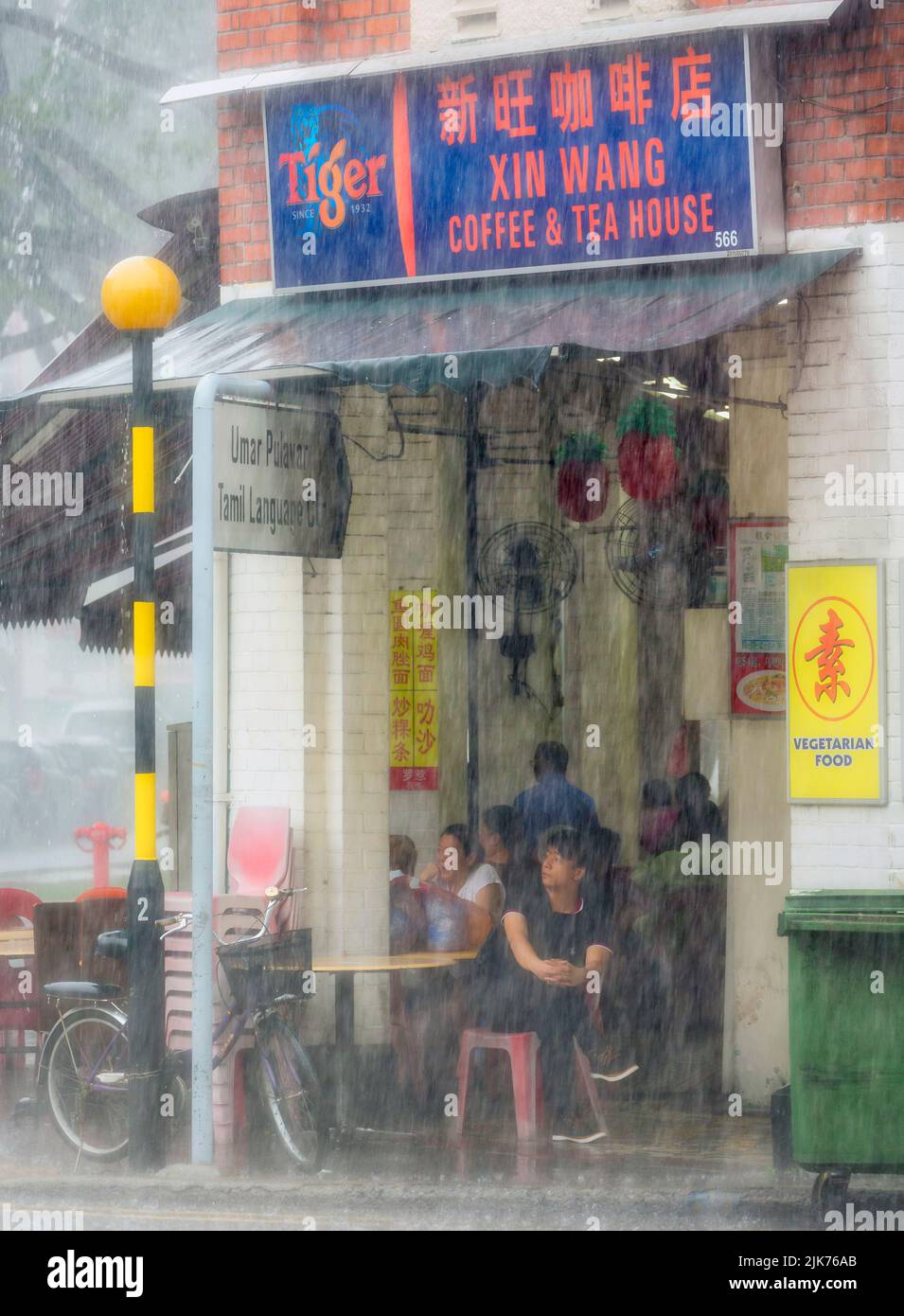 Customers in coffee and tea house waiting out tropical downpour on Serangoon Road, Republic of Singapore. Stock Photo