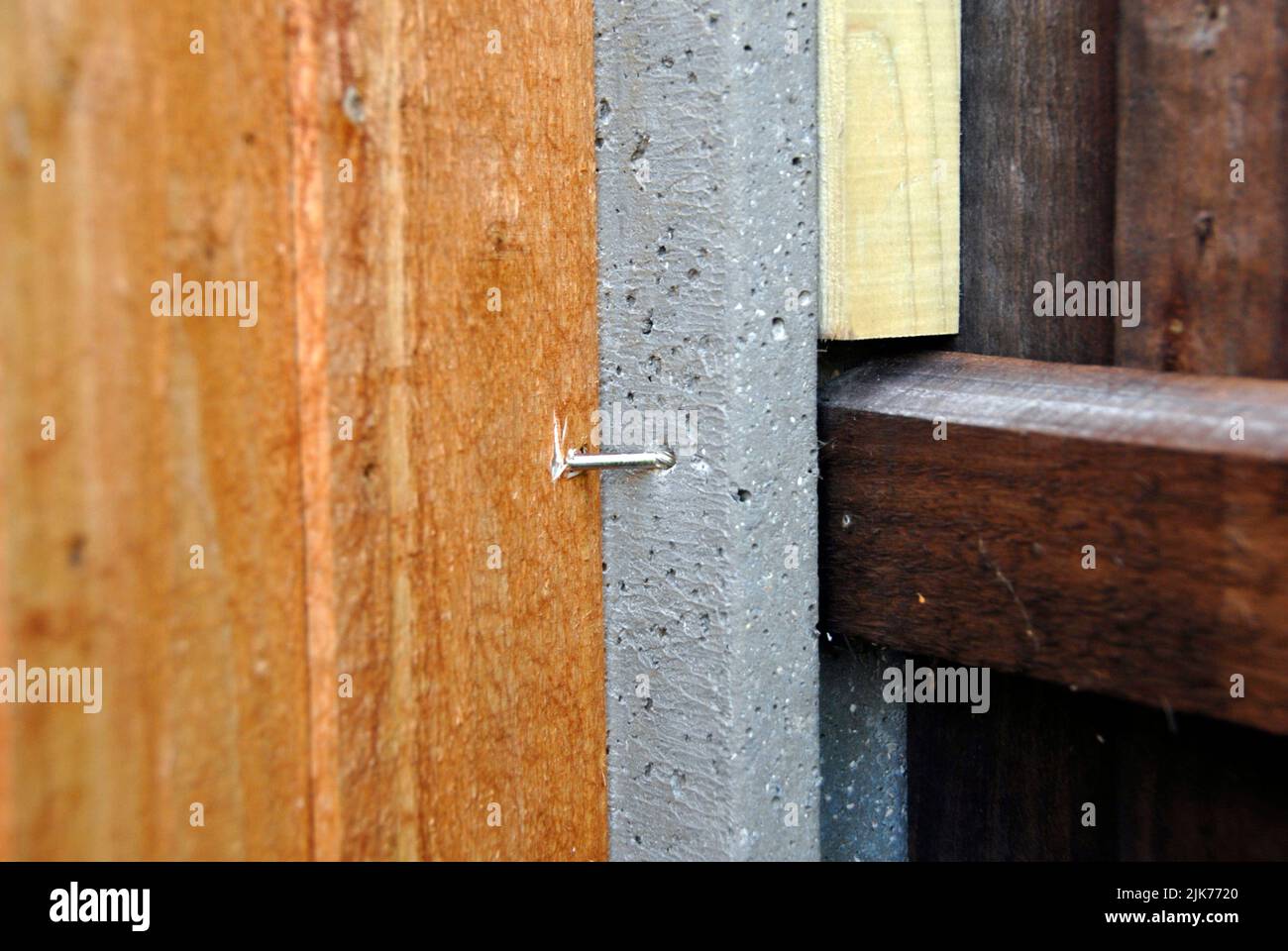 Wooden fence panel screwed to neighboring concrete fence post Stock Photo