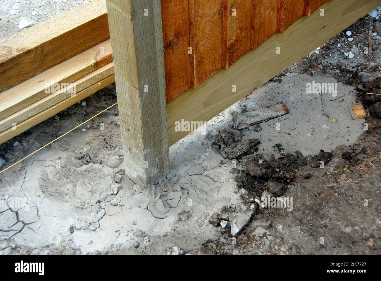 Wooden fence post set in quick-drying cement with fence panel attached and string for guide line visible Stock Photo