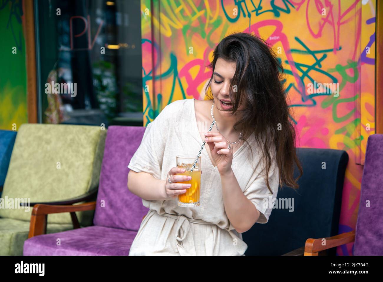 Happy young woman with a glass of lemonade against a bright painted wall. Stock Photo