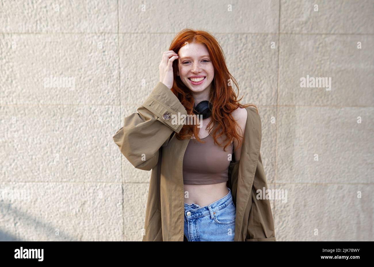 Happy teen redhead girl looking at camera standing on urban wall background. Stock Photo